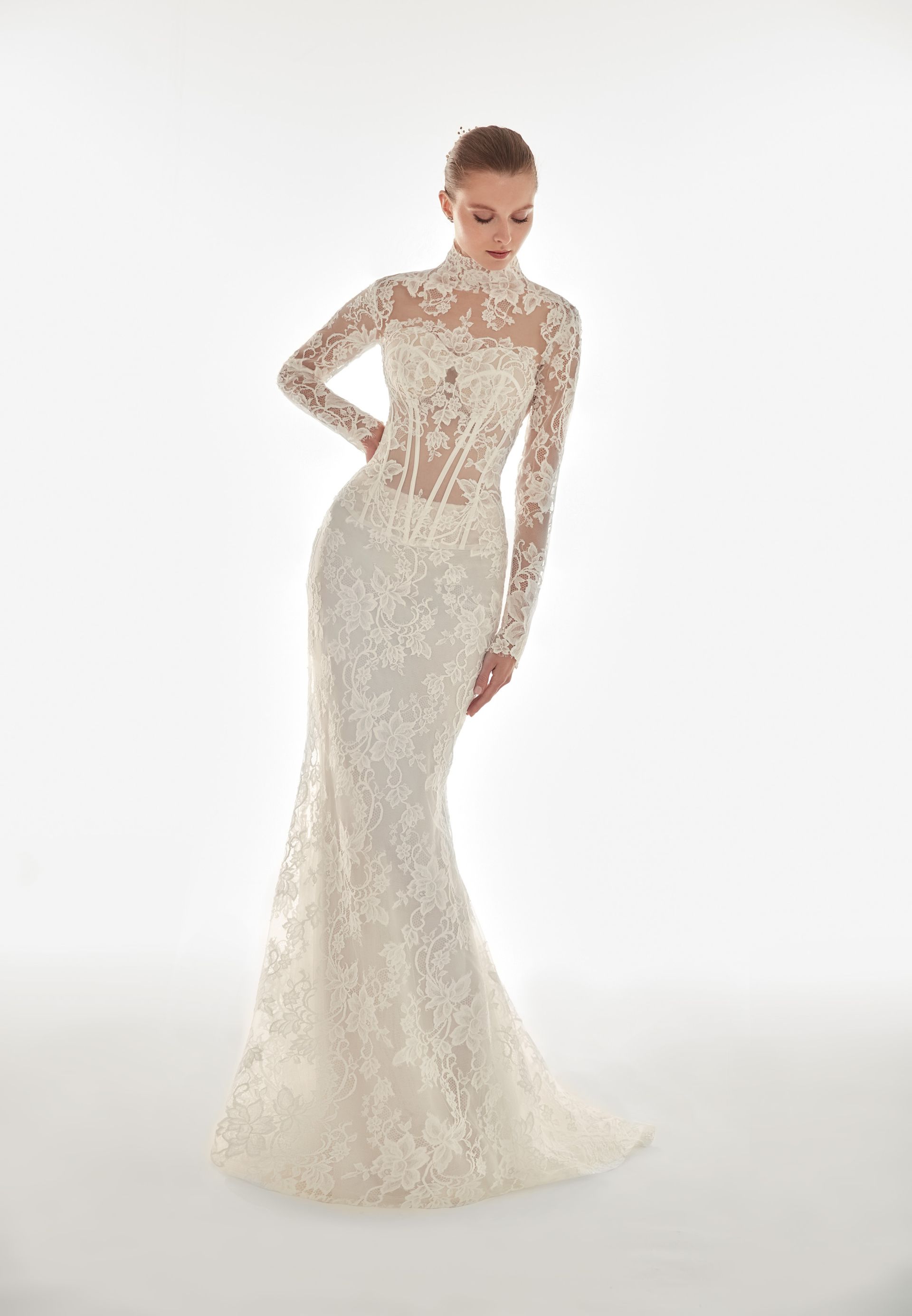 Donna in posa con abito da sposa in pizzo bianco, scollatura alta e maniche lunghe.