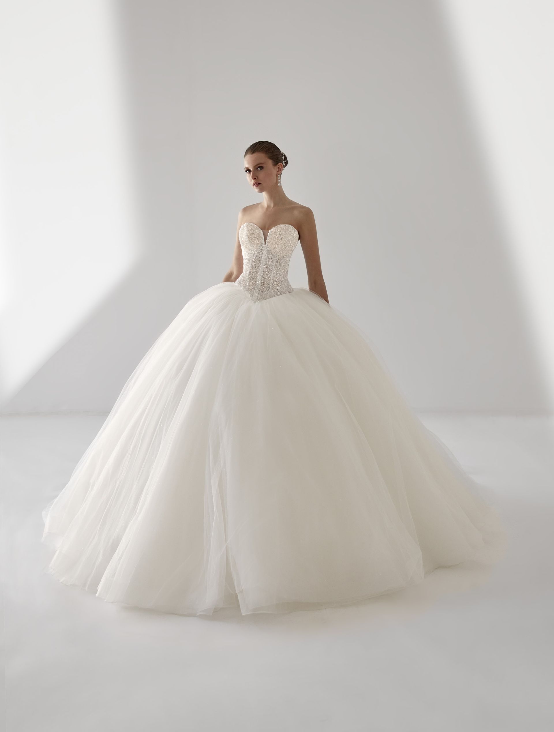 Abito da sposa bianco senza spalline con corpetto decorato con perline, donna in piedi in studio.