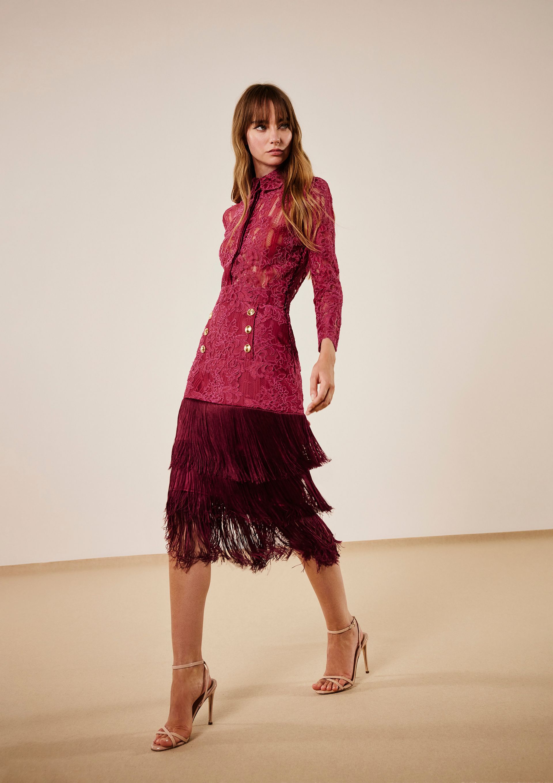 Donna che indossa un abito rosa con perline, orlo con frange e tacchi, in posa in uno studio.