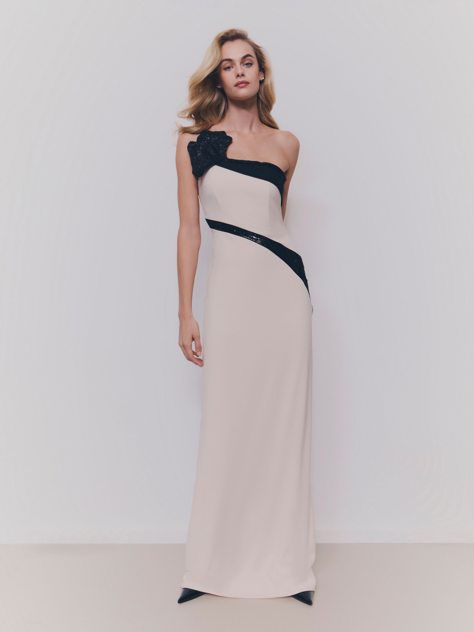 Donna che indossa un abito formale color crema, monospalla, con dettagli neri e un dettaglio floreale sulla spalla.