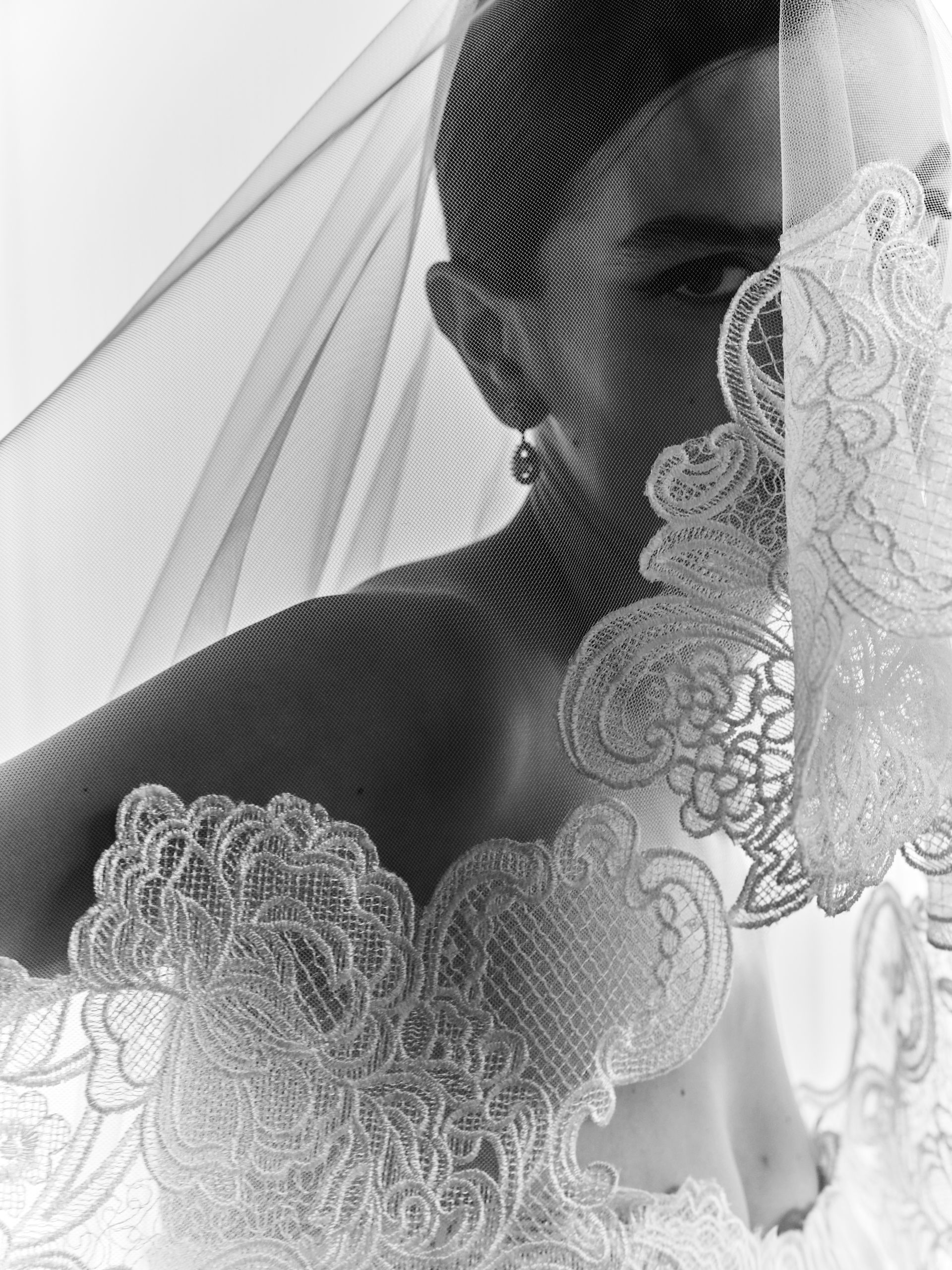 Silhouette della sposa velata, dettagli in pizzo che incorniciano il suo profilo laterale in bianco e nero.