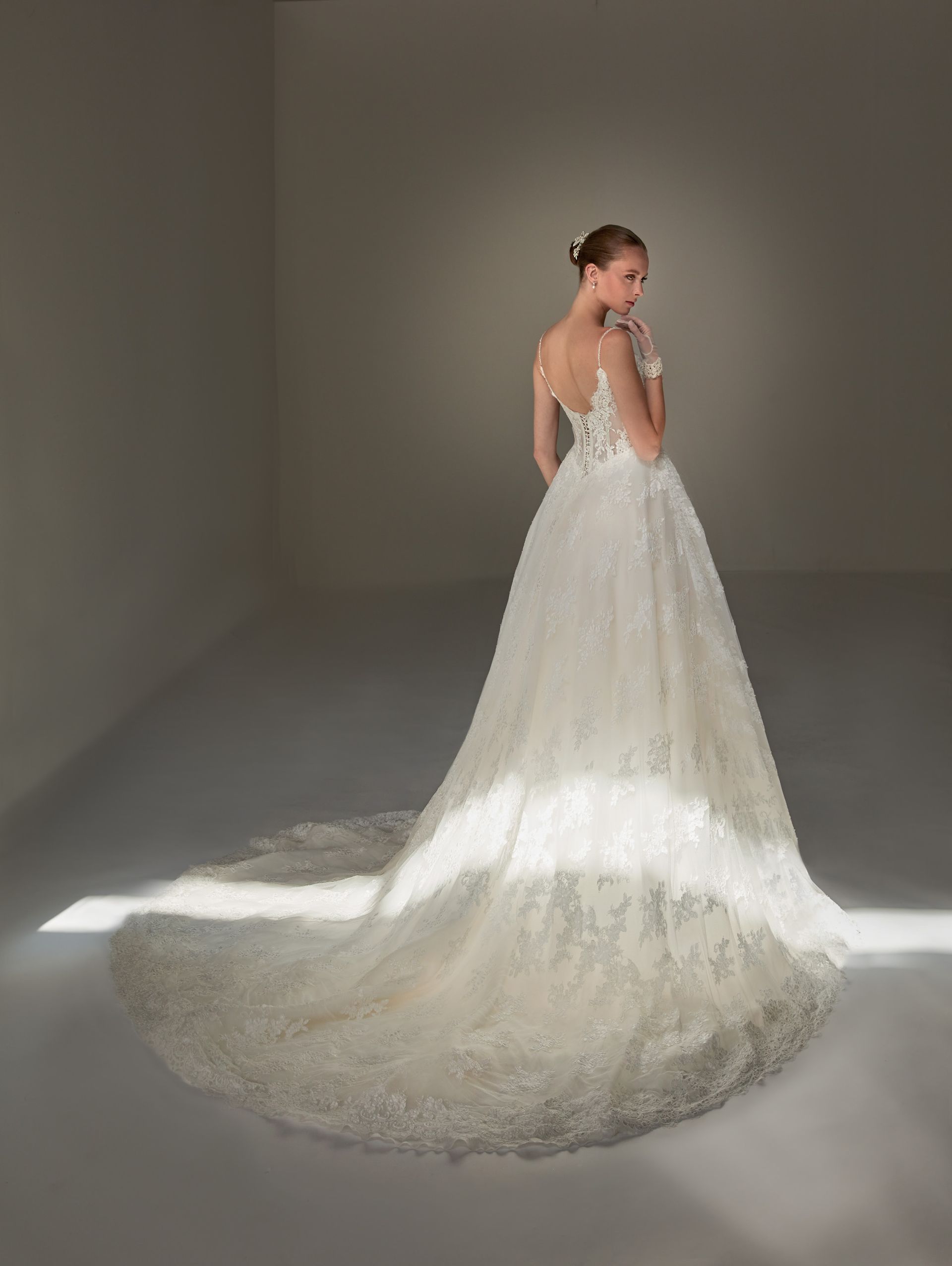 Donna in abito da sposa bianco, di spalle alla telecamera, con lo sguardo rivolto oltre le spalle, lungo strascico.