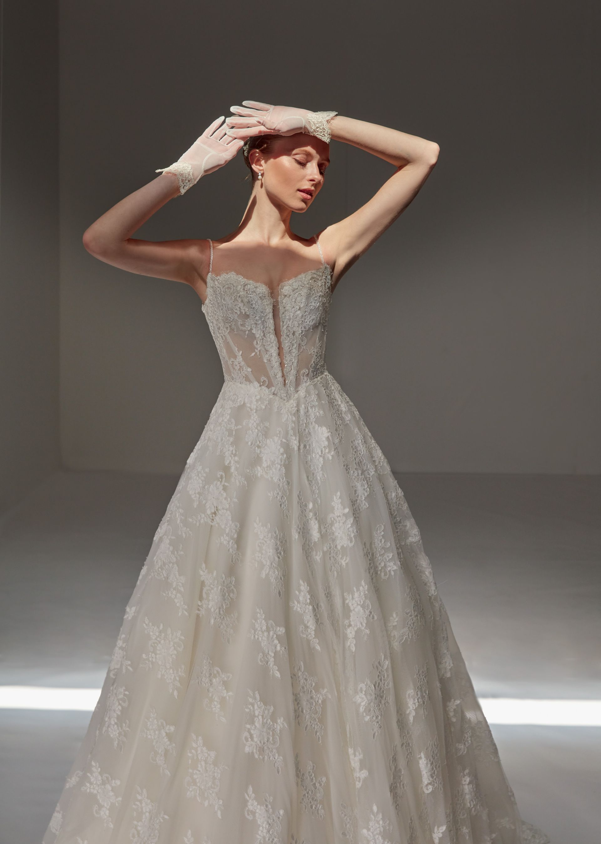 Donna in abito da sposa senza spalline decorato con perline, braccia alzate, guanti, in studio.