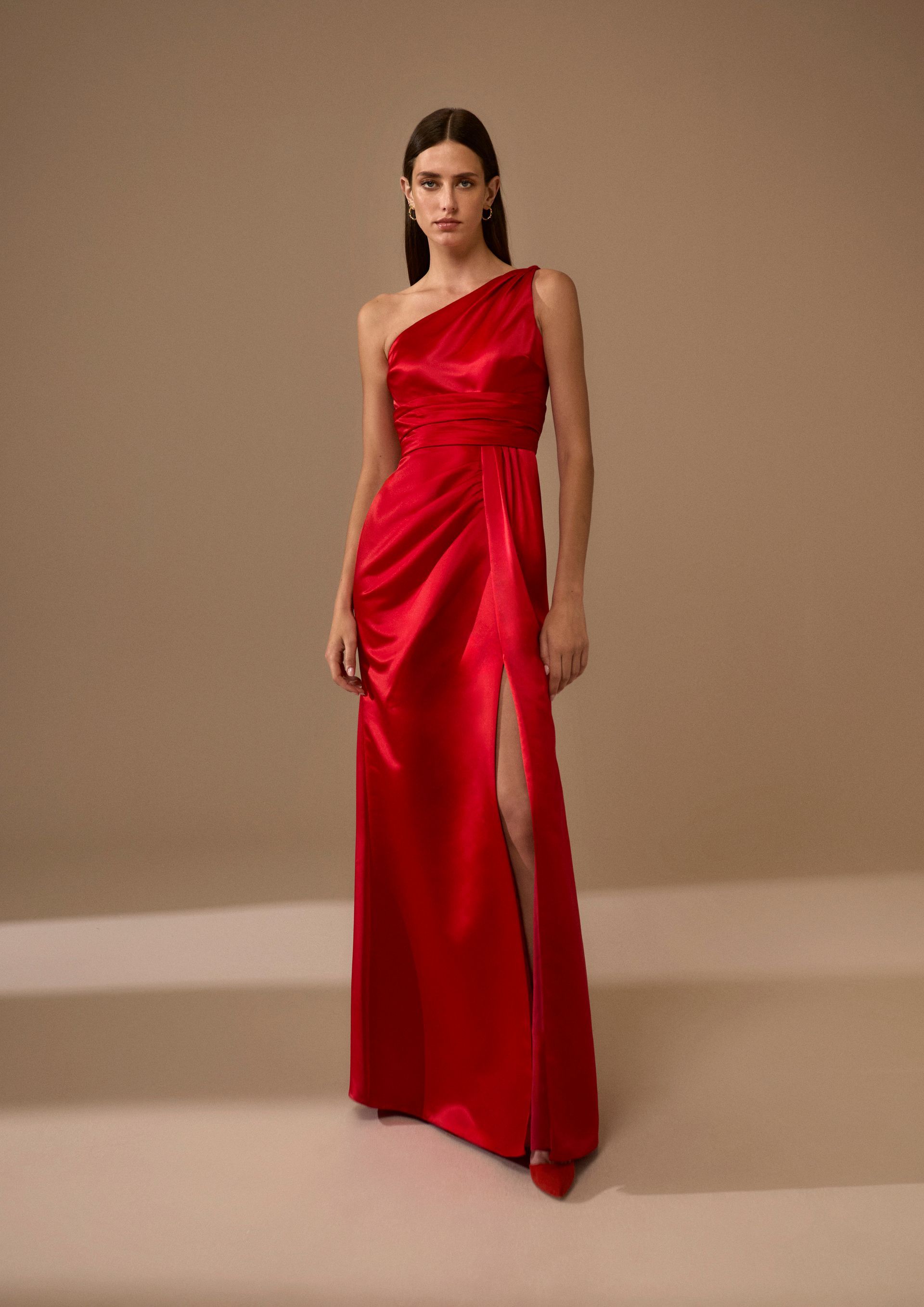 Donna in abito rosso monospalla con spacco profondo, in piedi in un interno.