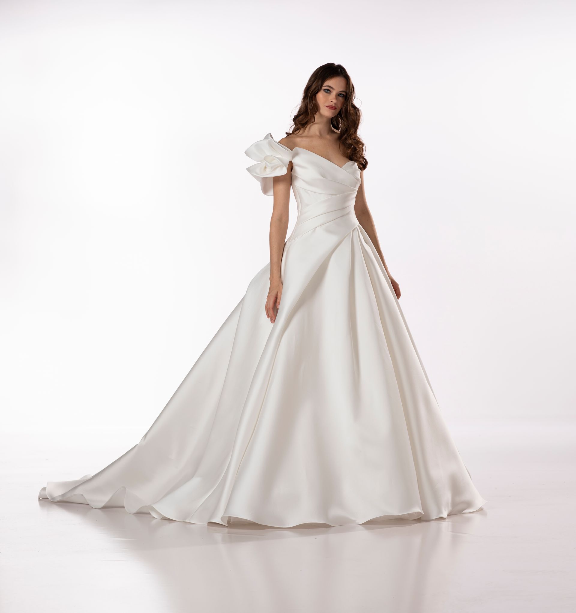 Donna in abito da sposa bianco con spalle scoperte e strascico, in posa in studio.