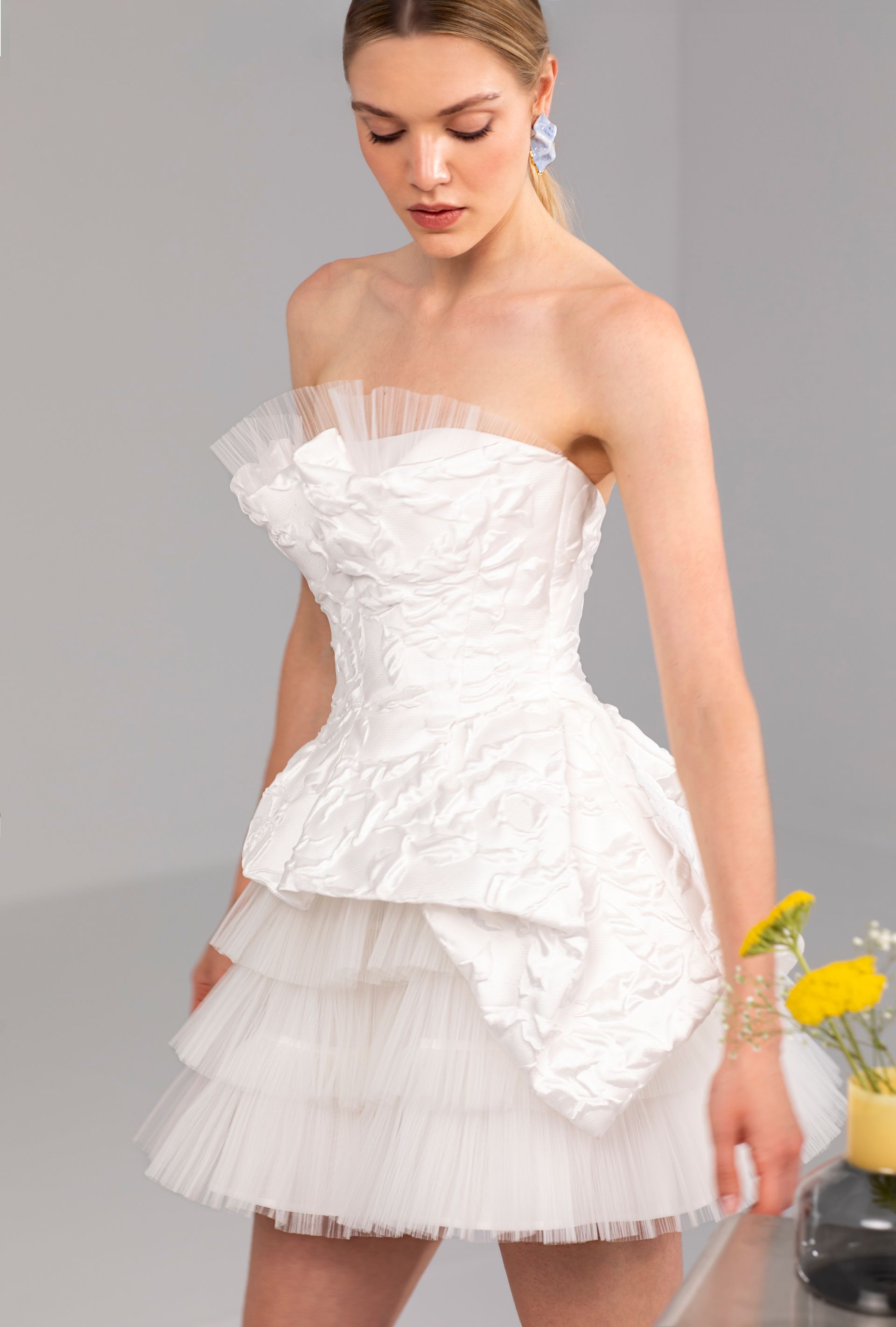 Donna che indossa un miniabito bianco testurizzato, senza spalline, con gonna a balze. 