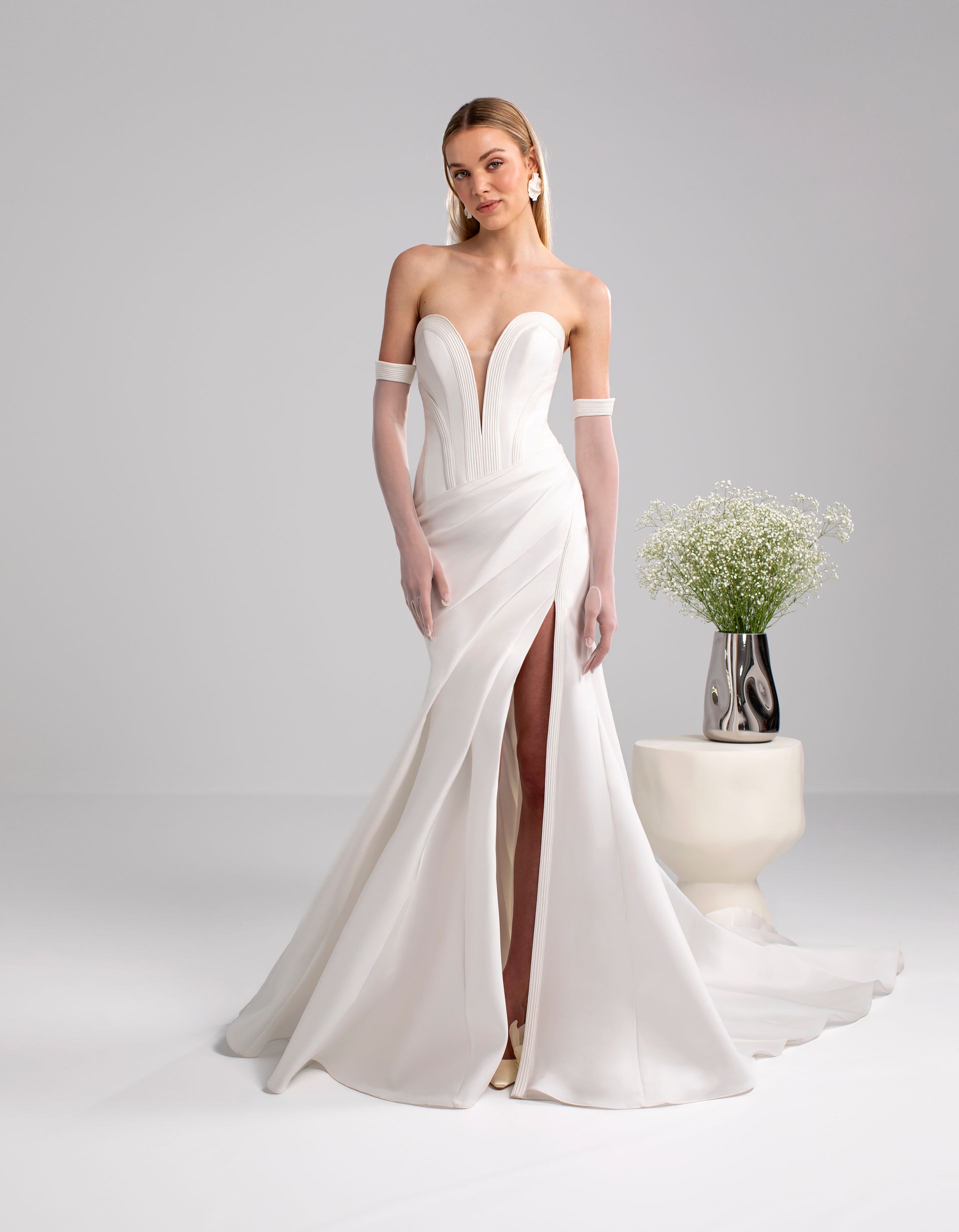 Donna che indossa un abito da sposa bianco senza spalline con uno spacco profondo, in posa in un interno.