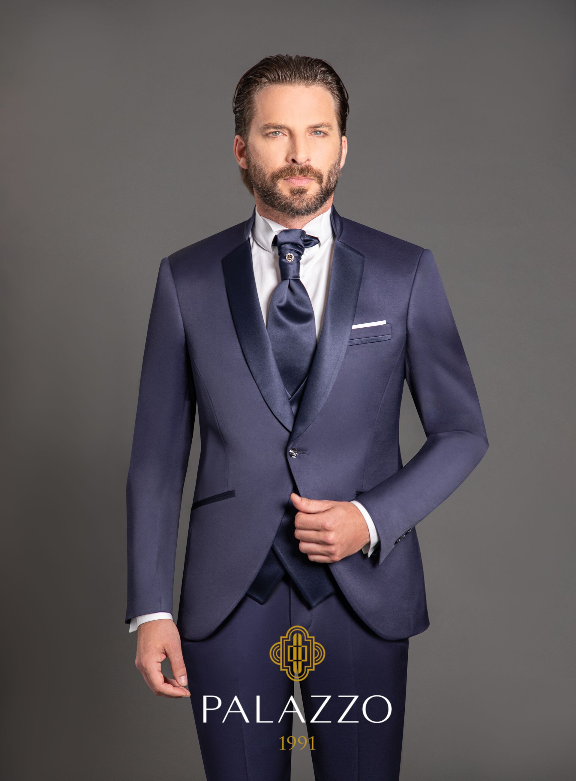 Uomo in abito blu navy con gilet e cravatta, in posa davanti a uno sfondo grigio.