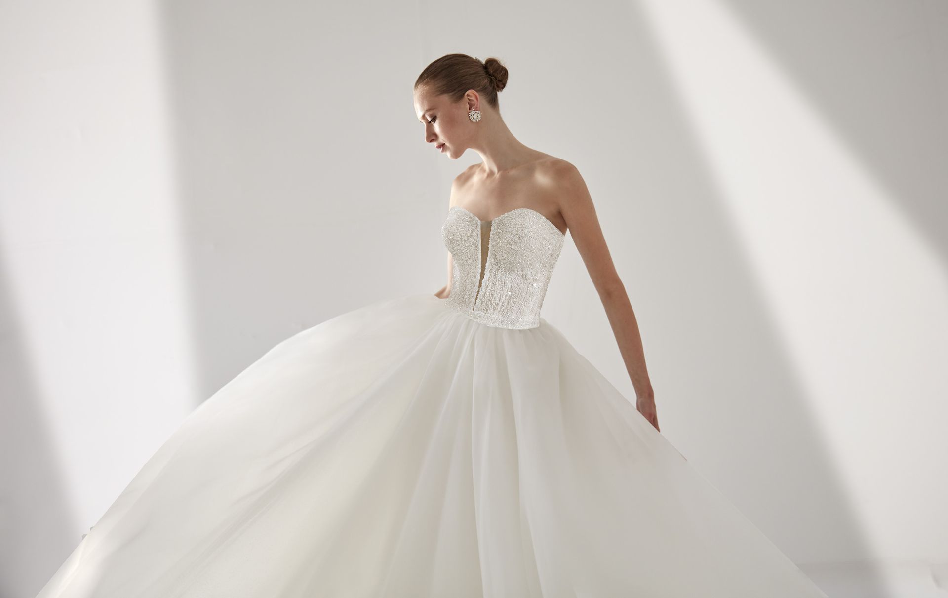 Donna in abito da sposa bianco senza spalline, gonna a palloncino, con sguardo rivolto verso il basso, in studio.