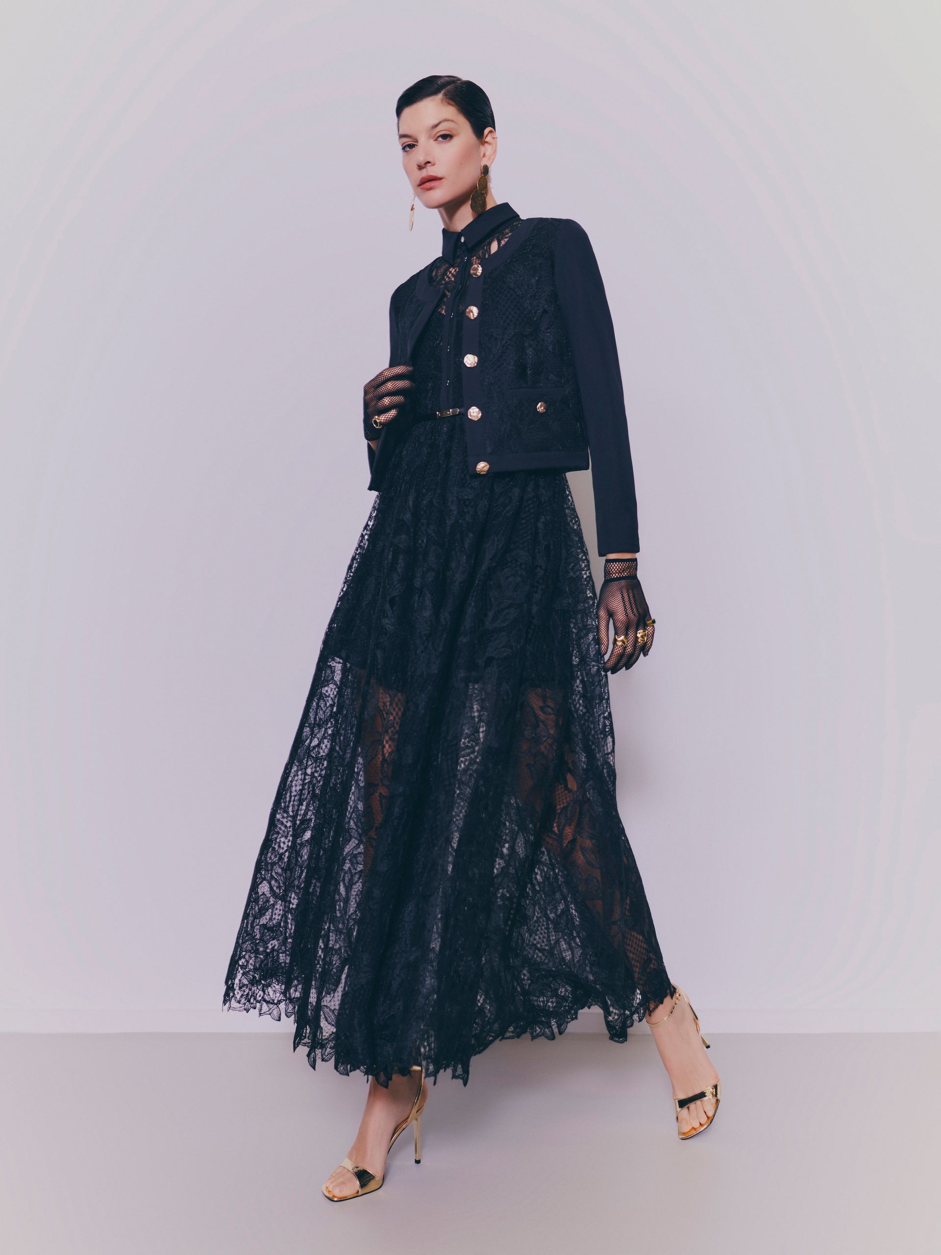 Donna con giacca nera e gonna di pizzo, indossa guanti e tacchi.