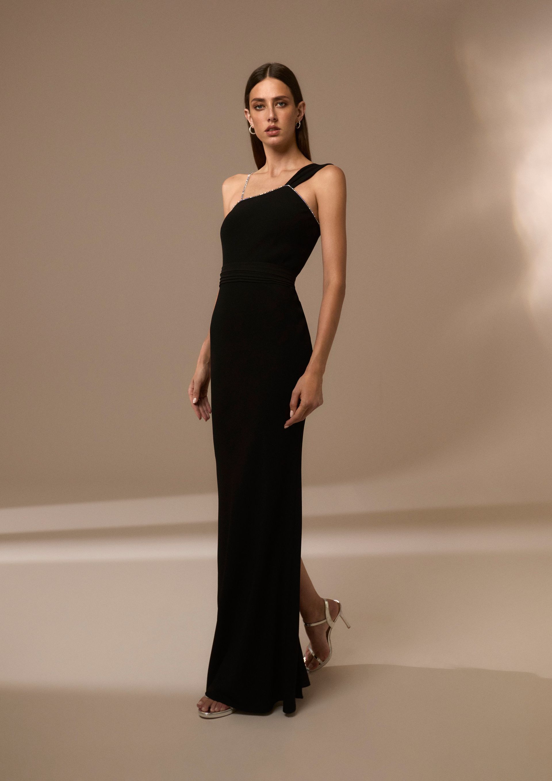 Donna con abito nero monospalla con spacco; in piedi in uno studio, indossa tacchi.