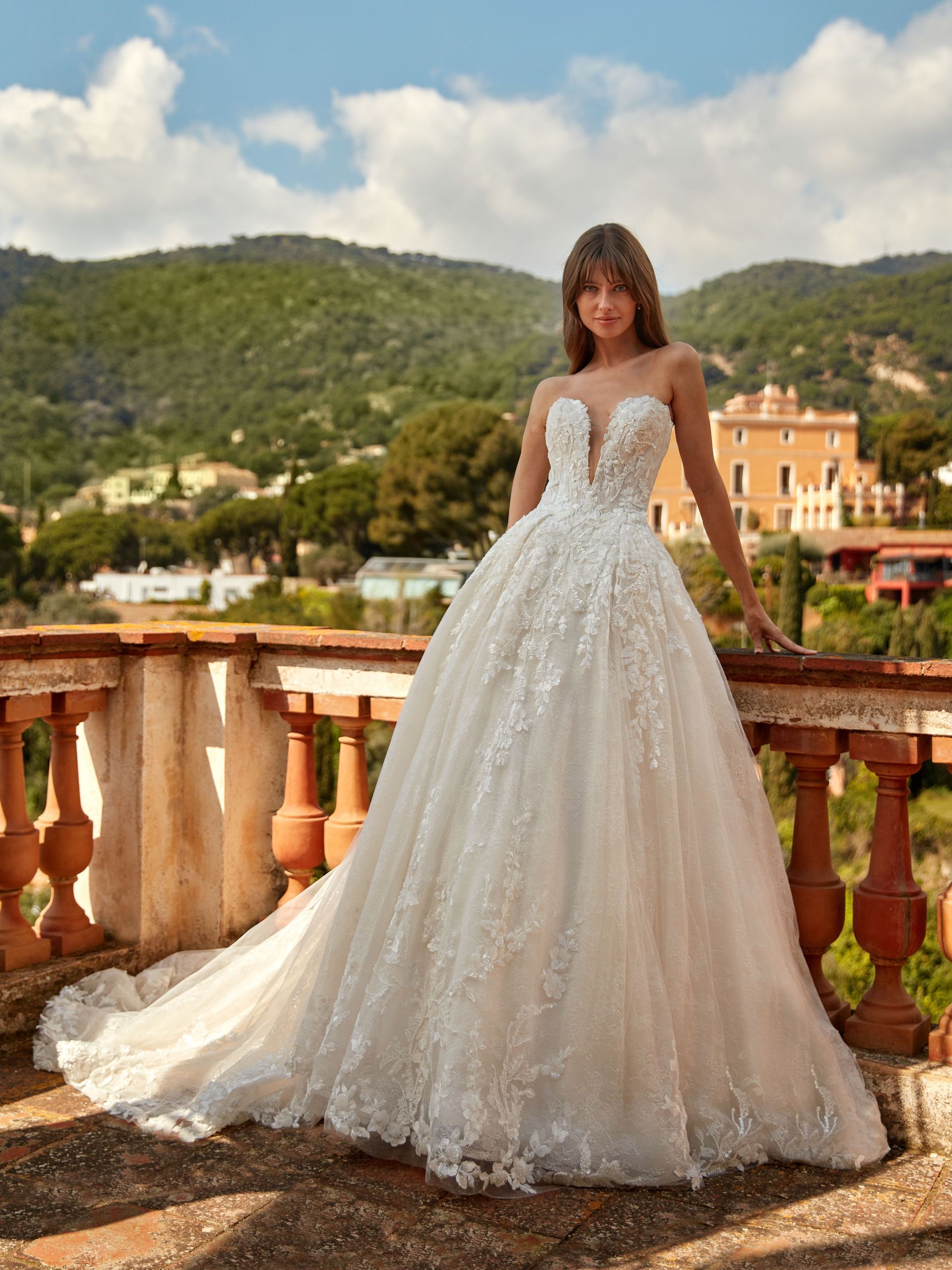 Donna in abito da sposa bianco senza spalline con decorazioni floreali, in piedi su un balcone