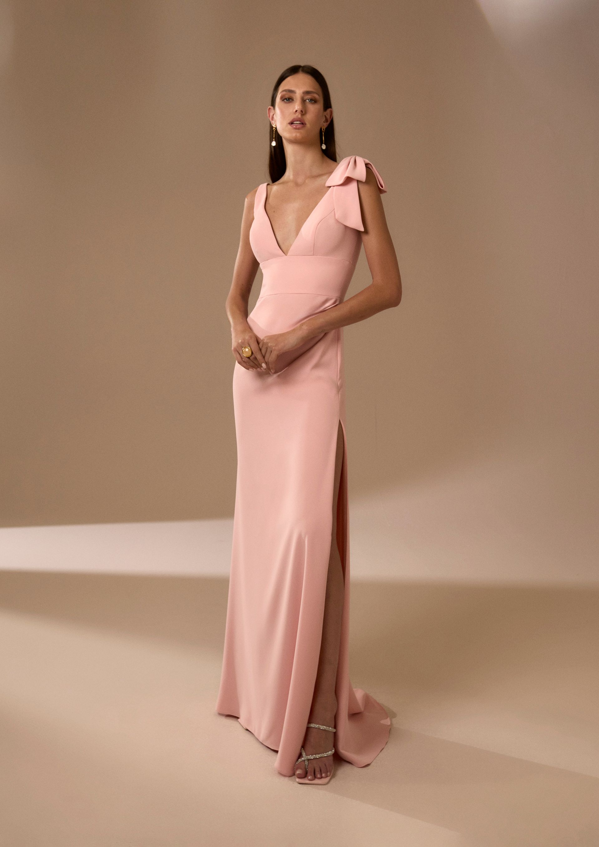 Donna in abito rosa con spacco profondo, in posa in un interno.