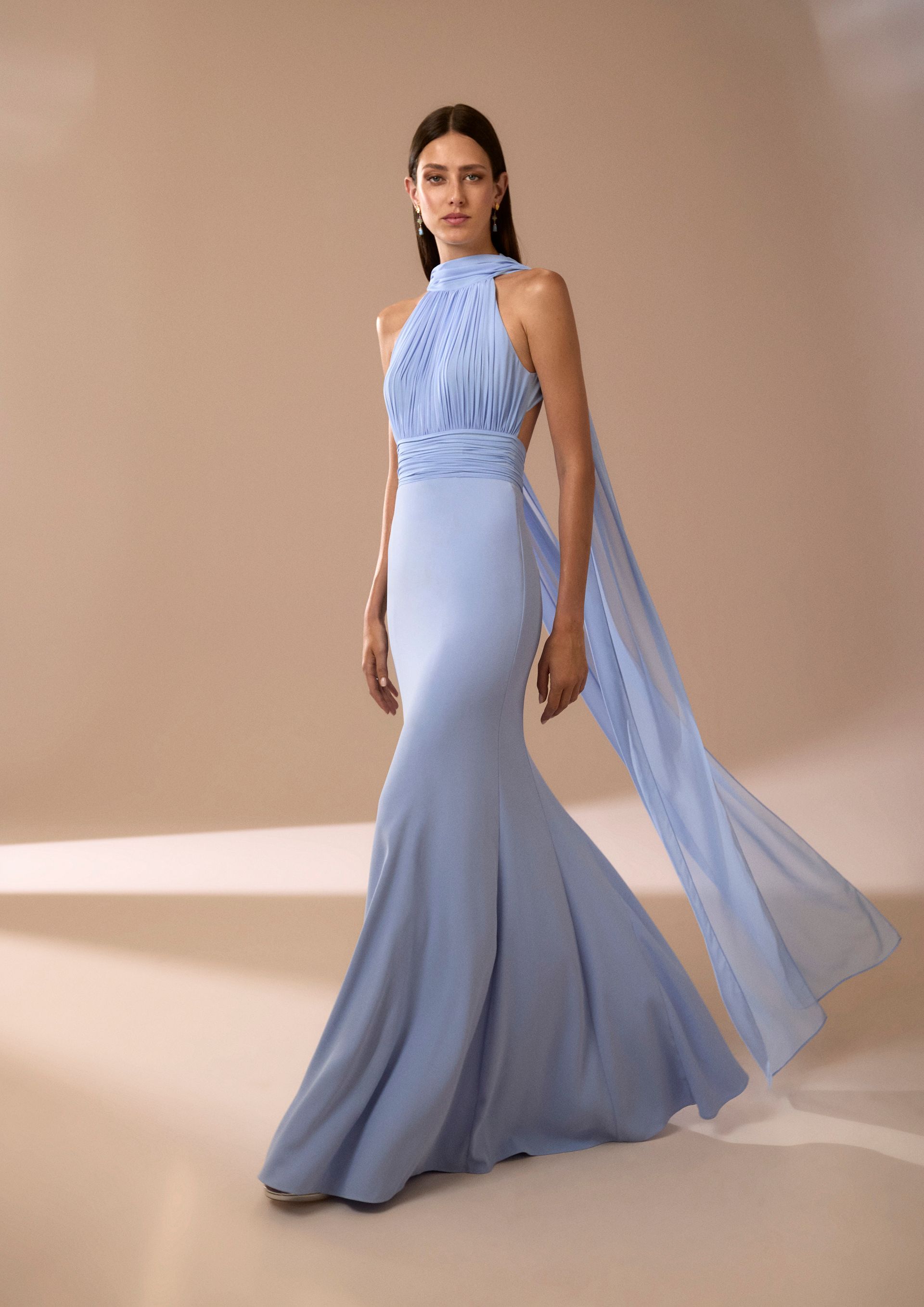 Donna in abito formale azzurro con mantello svolazzante, in piedi in uno studio fotografico.