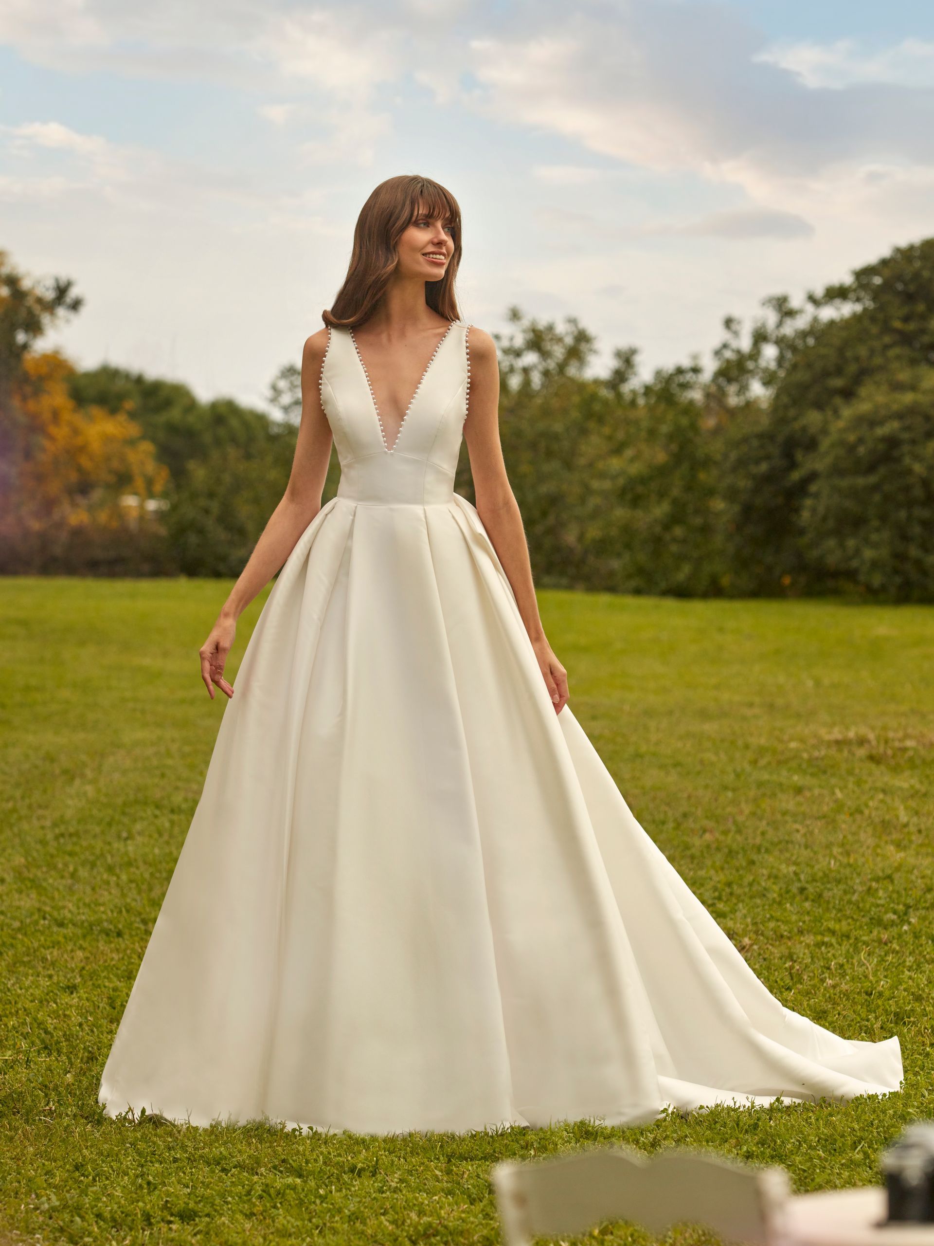 Donna in abito da sposa bianco, in piedi in un campo erboso, sorridente.