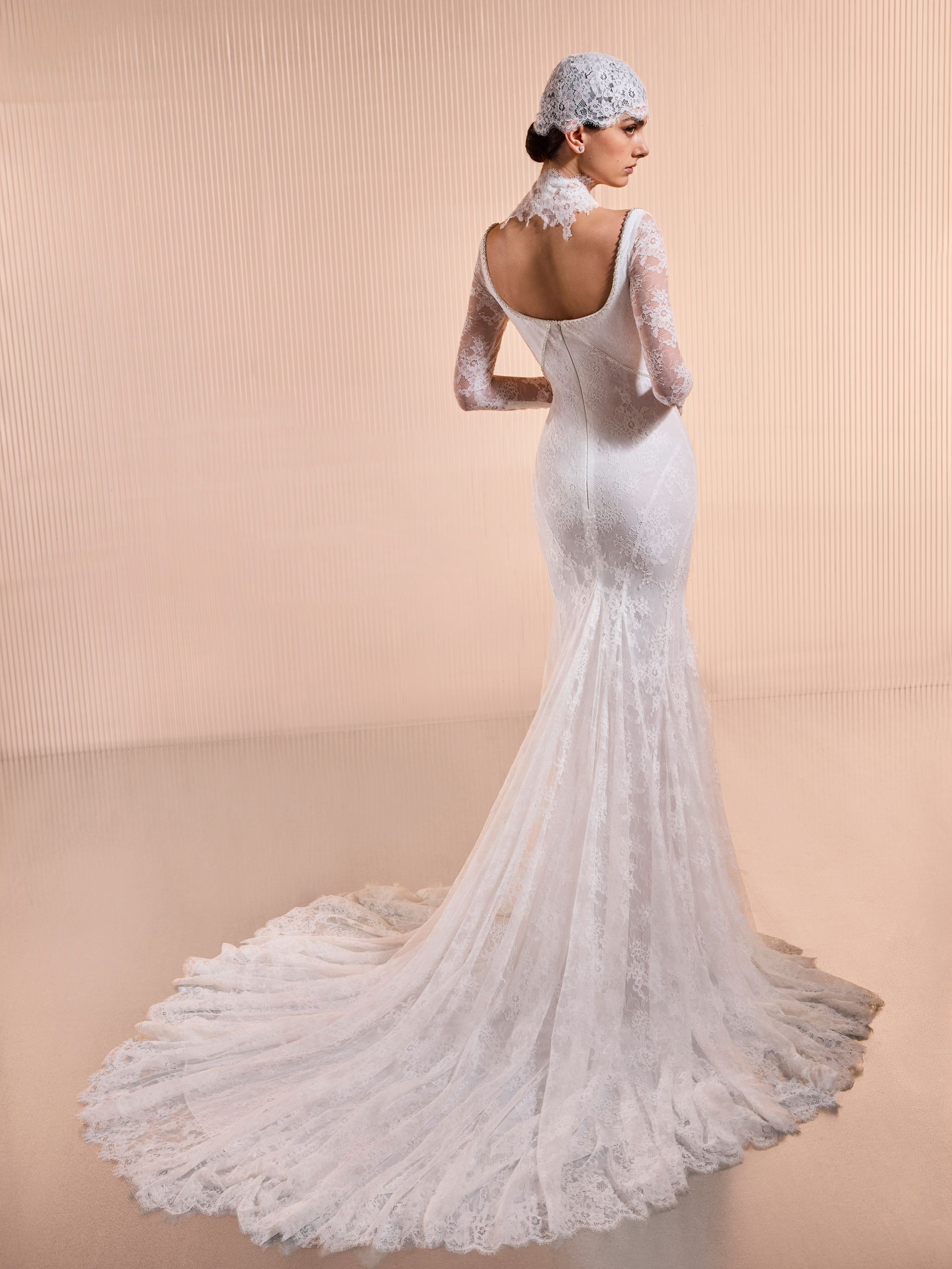 Donna in abito da sposa in pizzo bianco con lungo strascico, voltata dall'altra parte.