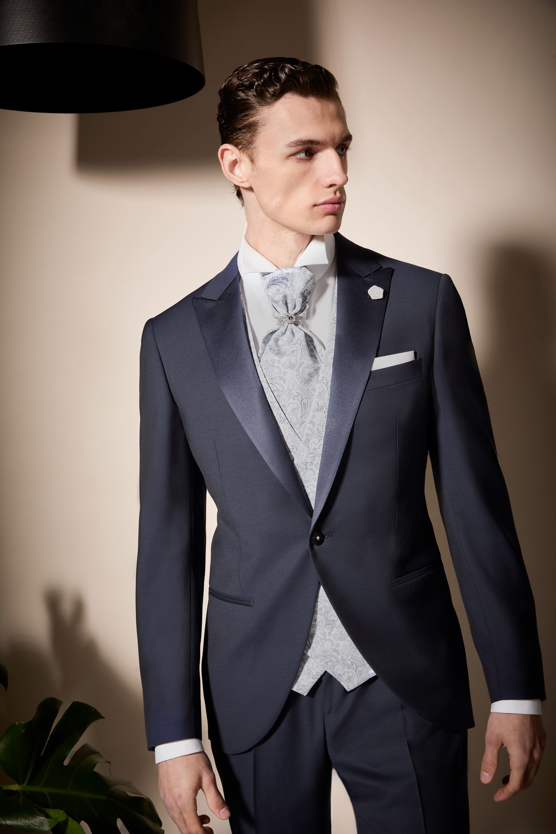 Uomo in abito formale blu scuro, gilet chiaro e cravatta, che guarda di lato.