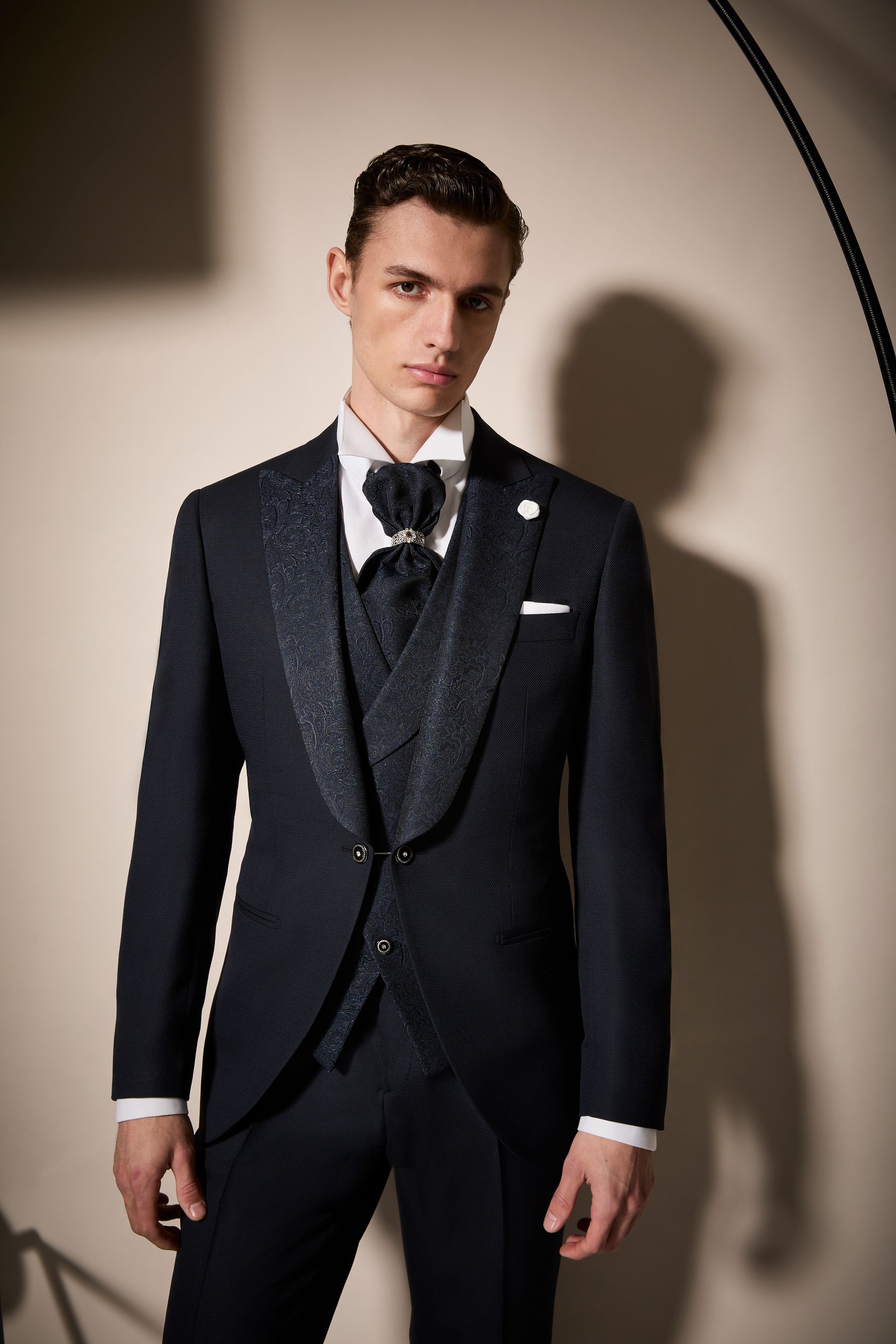 Uomo in abito scuro con papillon e gilet, in posa in studio.