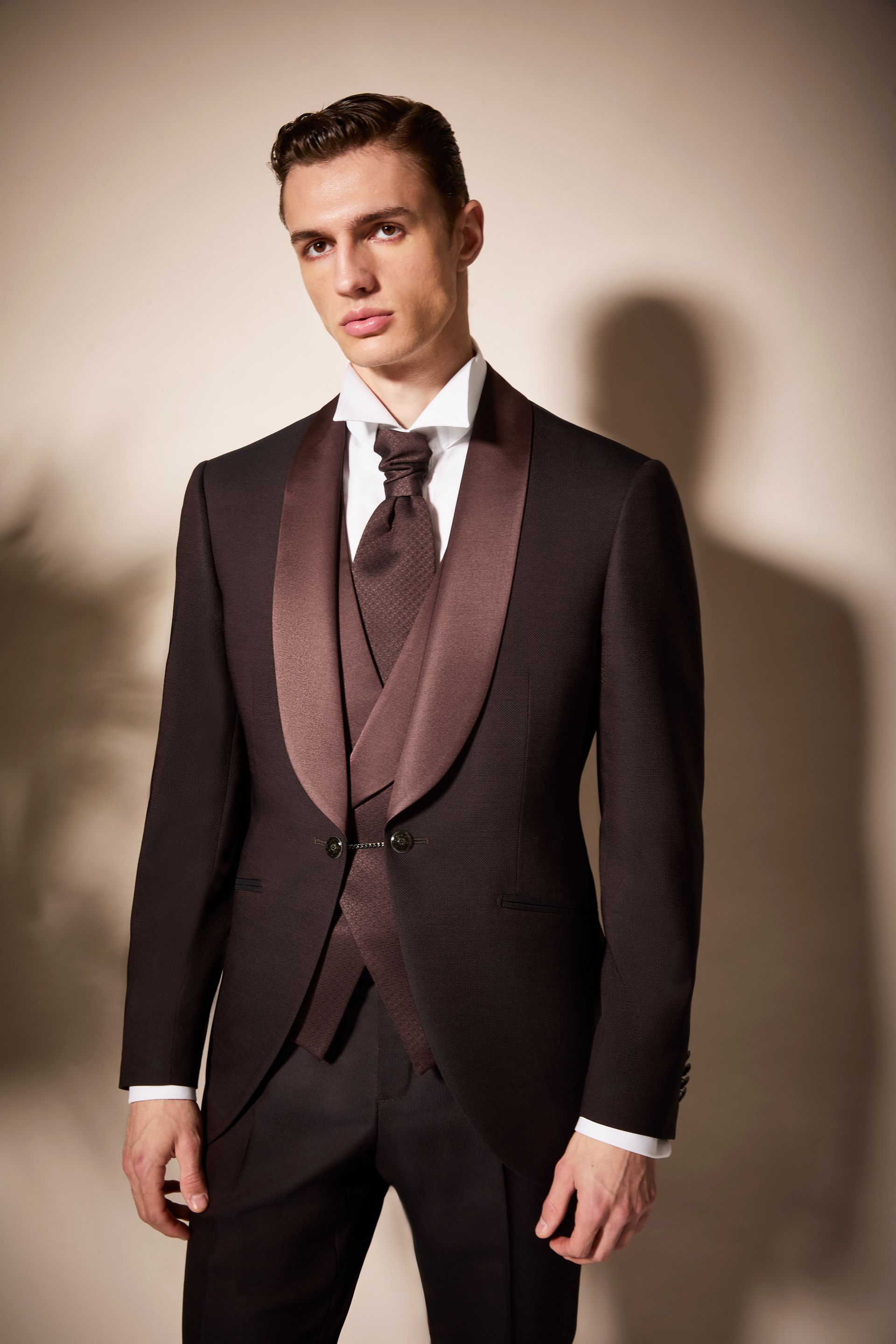 Uomo in smoking marrone scuro con risvolto e gilet in raso marrone chiaro, camicia bianca e cravatta.