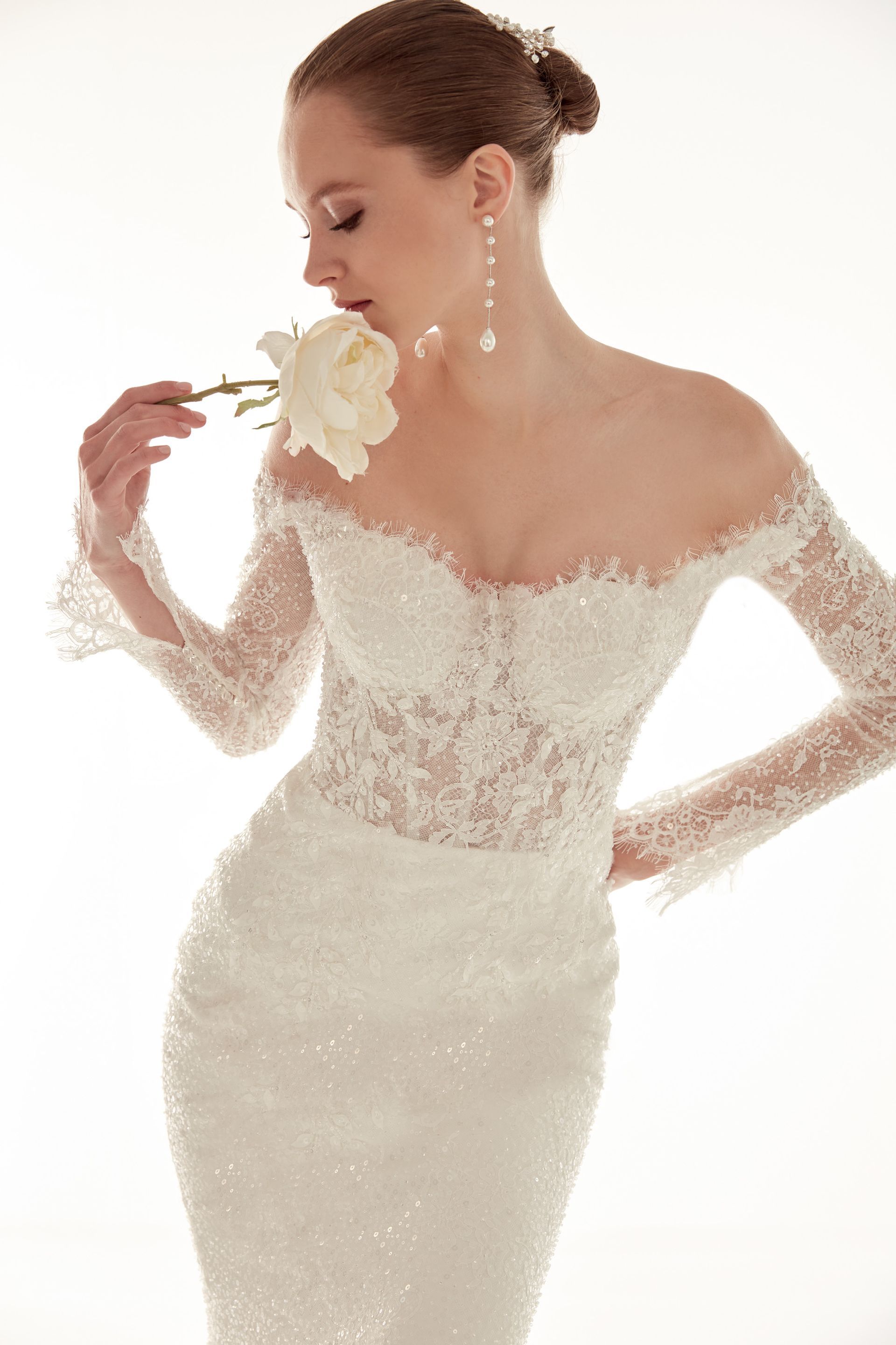 Donna con abito da sposa in pizzo bianco, che tiene in mano una rosa bianca e la annusa.