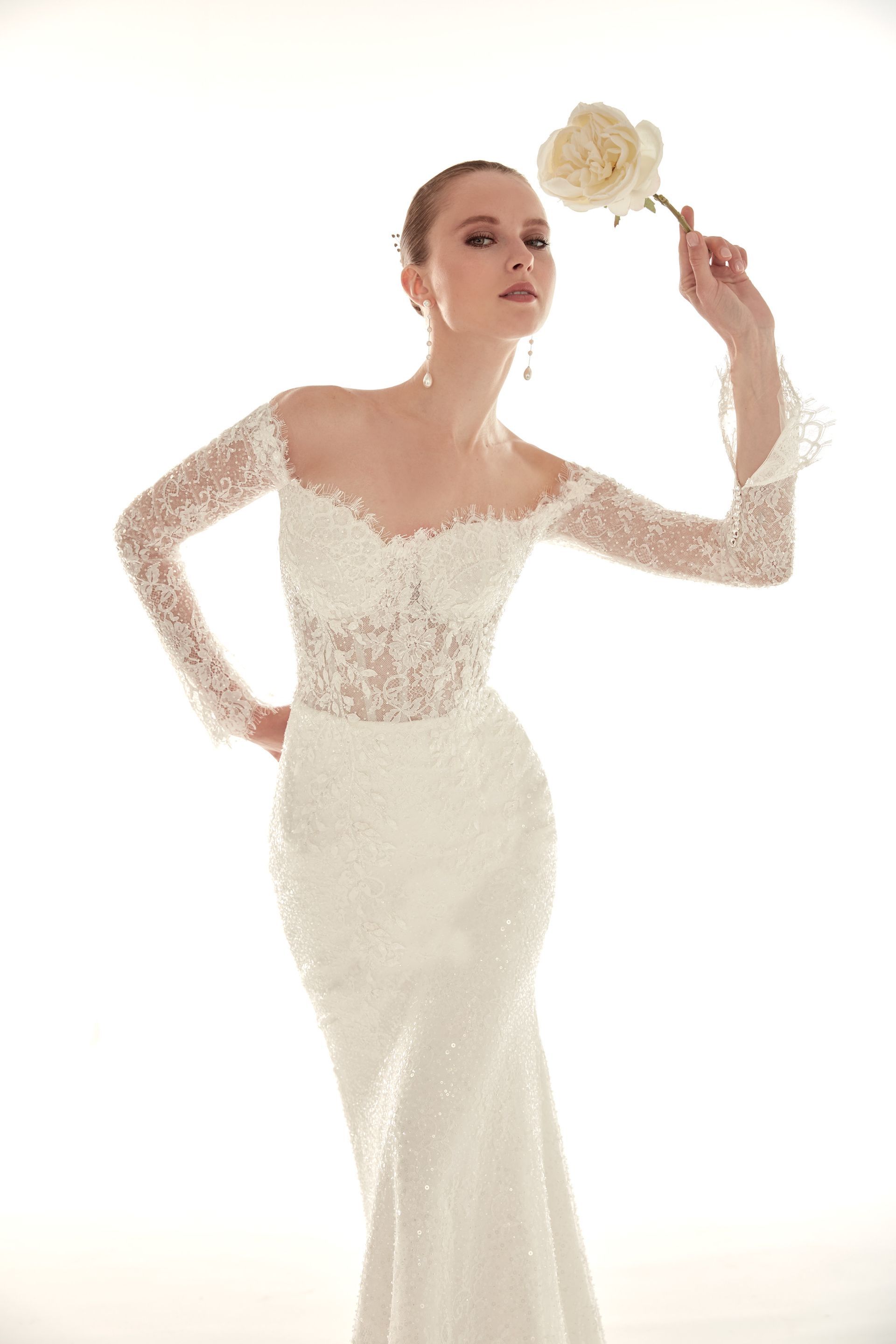 Una donna in abito da sposa bianco con perline tiene in mano una rosa e posa in studio.
