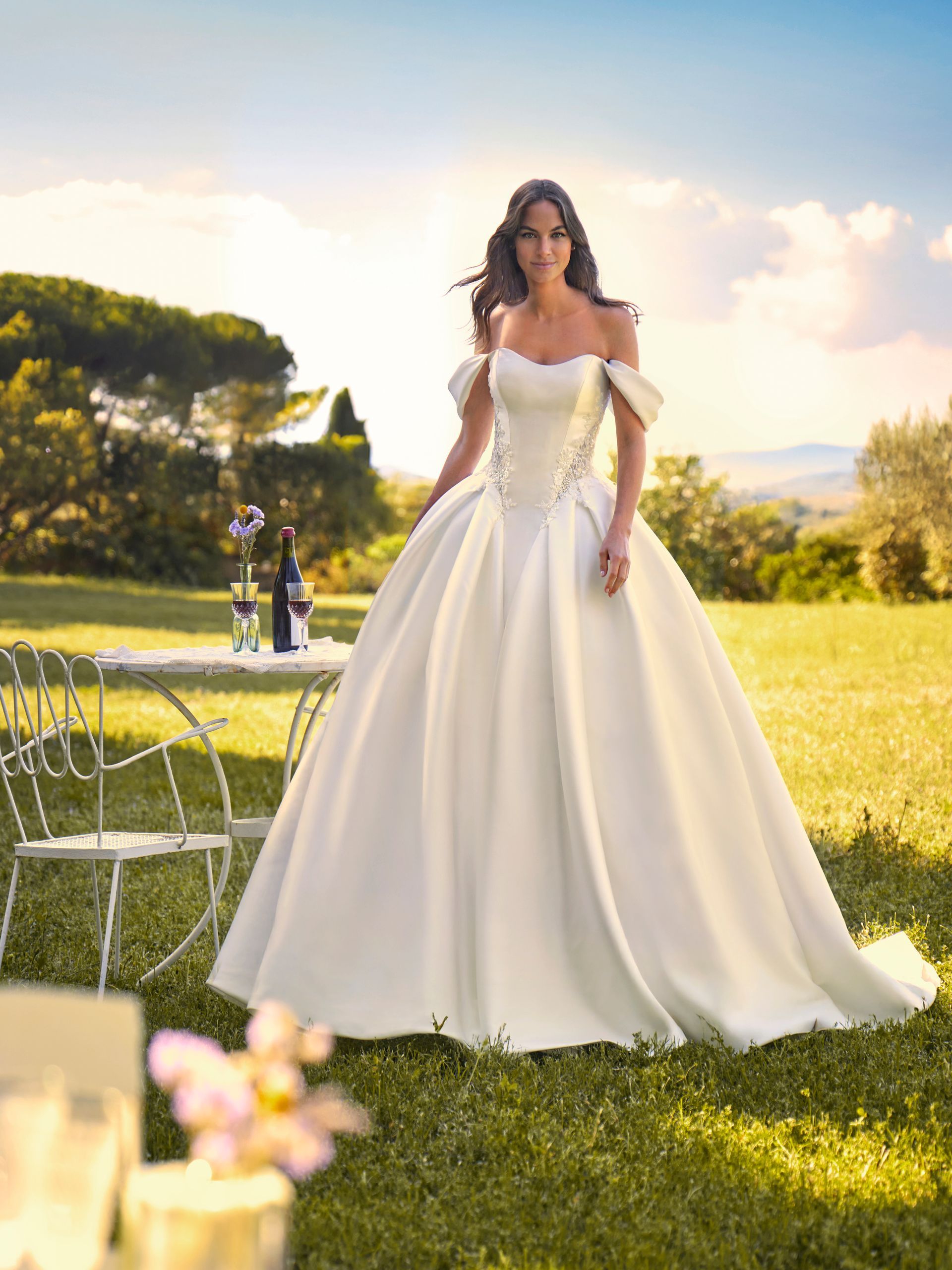 Donna con un abito da sposa bianco a spalle scoperte in piedi in un giardino soleggiato