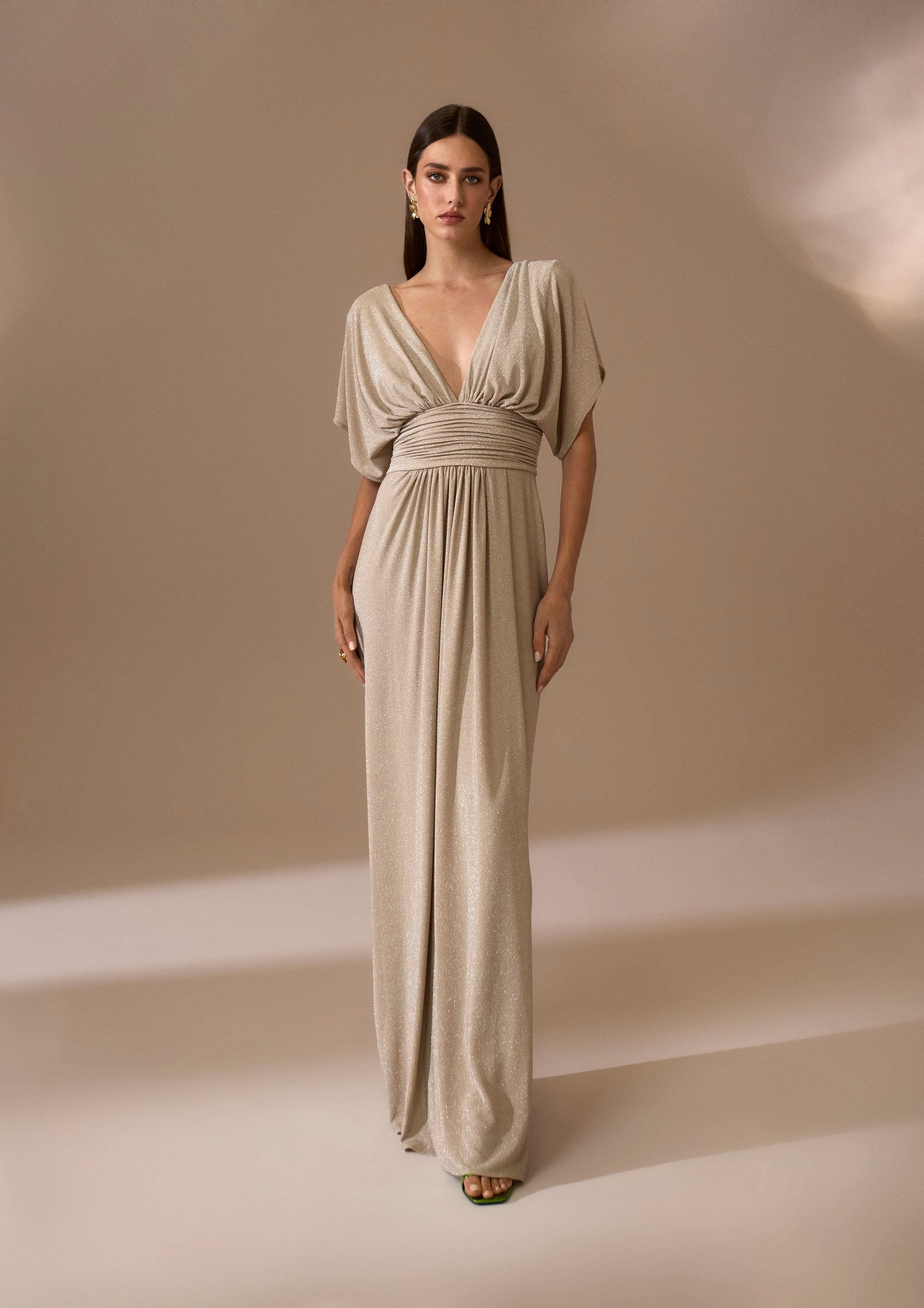 Donna in abito dorato scintillante, profonda scollatura a V, maniche corte, in posa in studio.