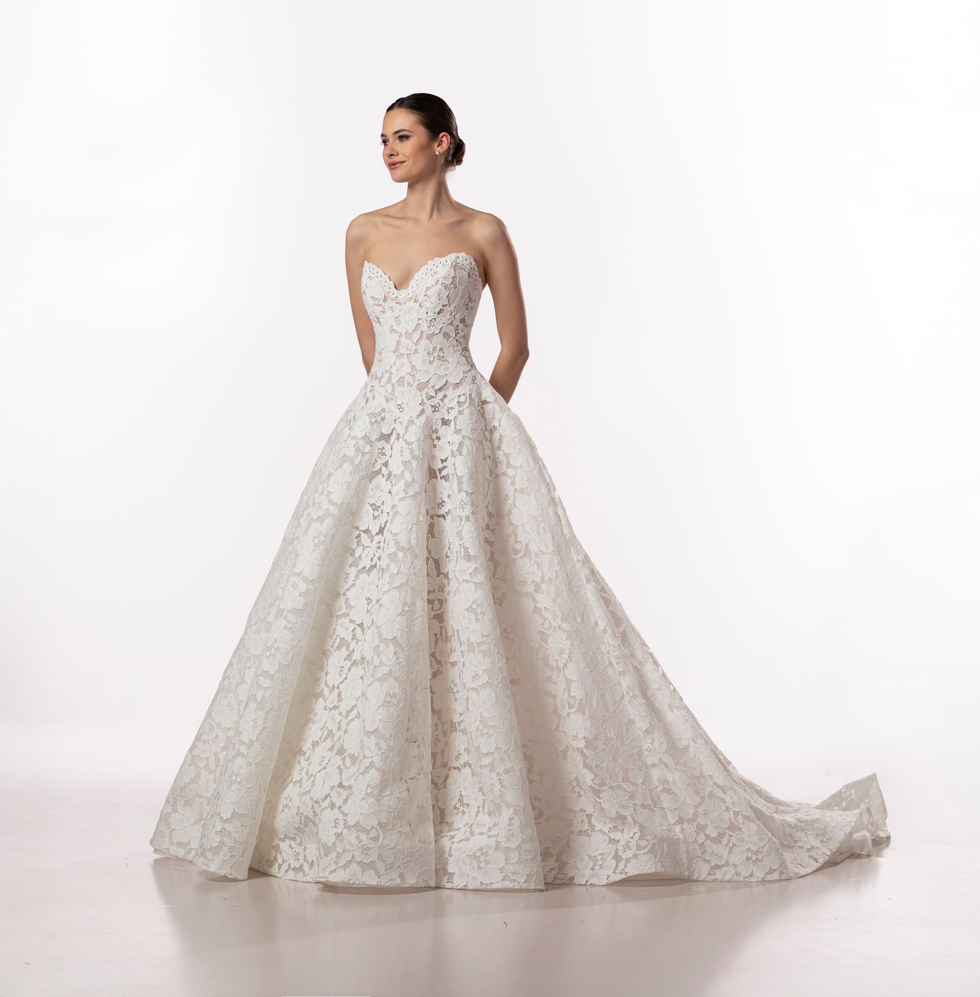 Donna con abito da sposa bianco senza spalline con motivo floreale in pizzo, che guarda di lato.