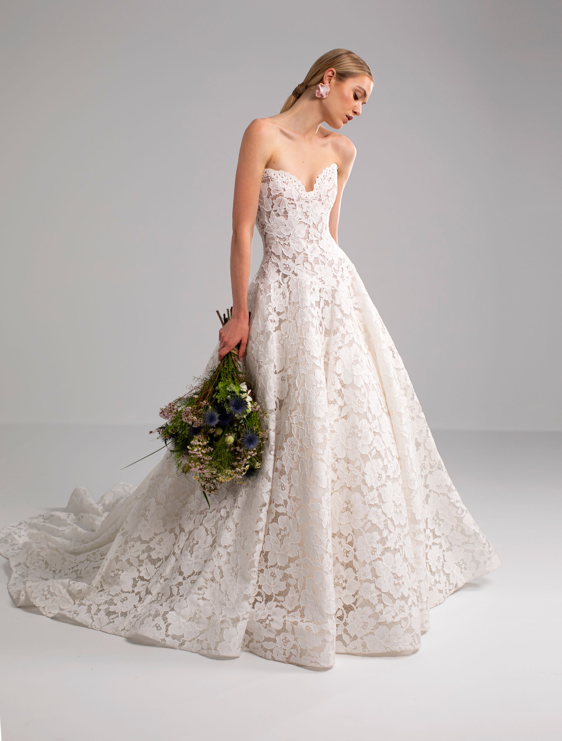 Donna in abito da sposa in pizzo senza spalline, con in mano un bouquet, in studio.