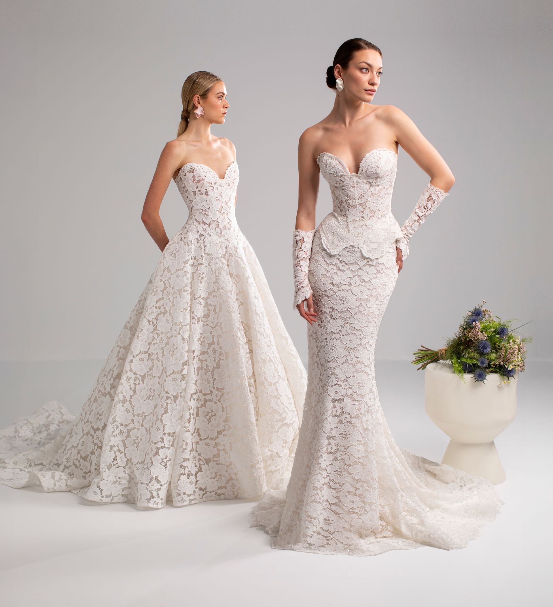 Due donne in abiti da sposa in pizzo bianco posano in studio.