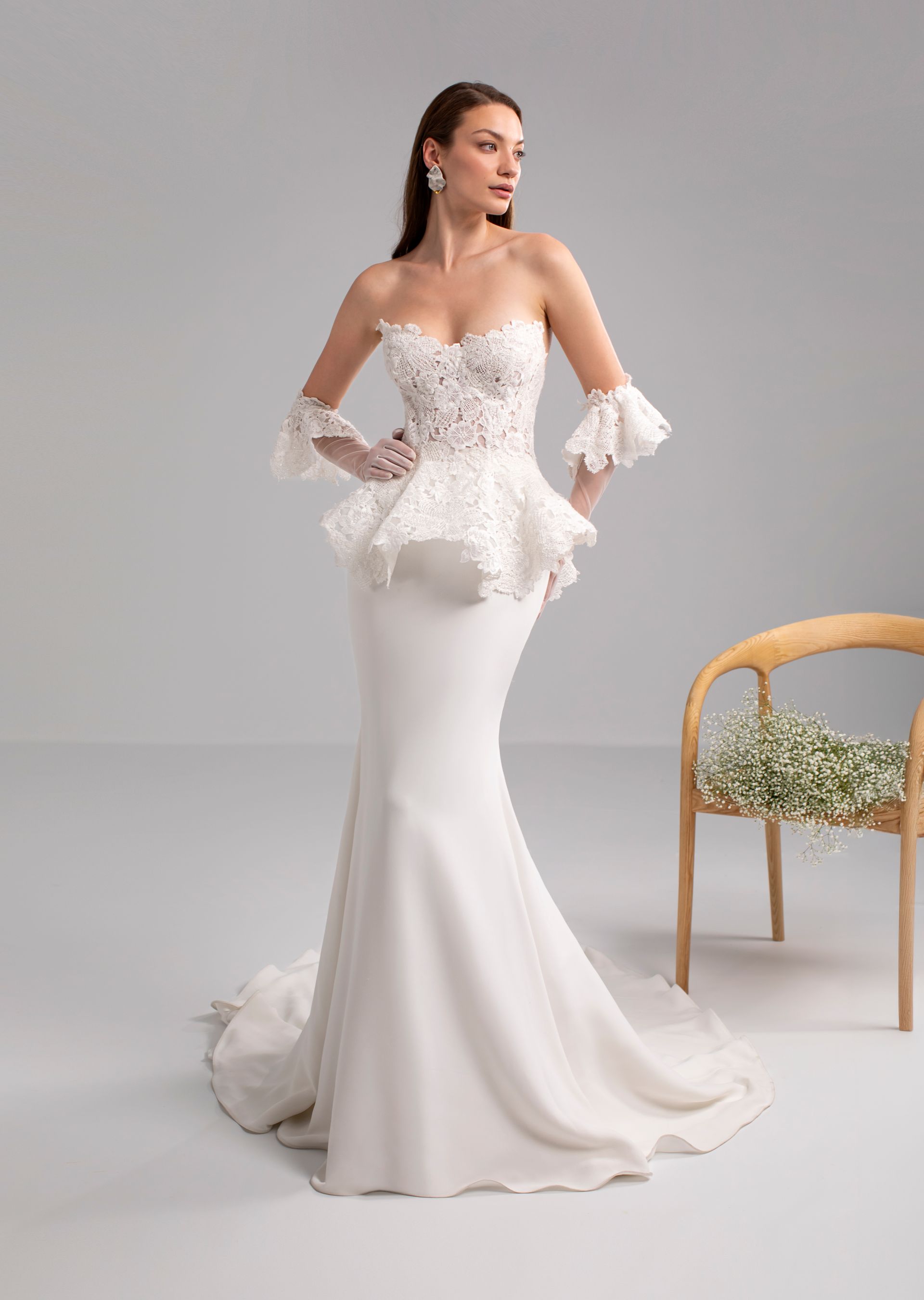 Donna in posa con abito da sposa bianco a sirena senza spalline, con corpetto in pizzo, peplo e maniche.