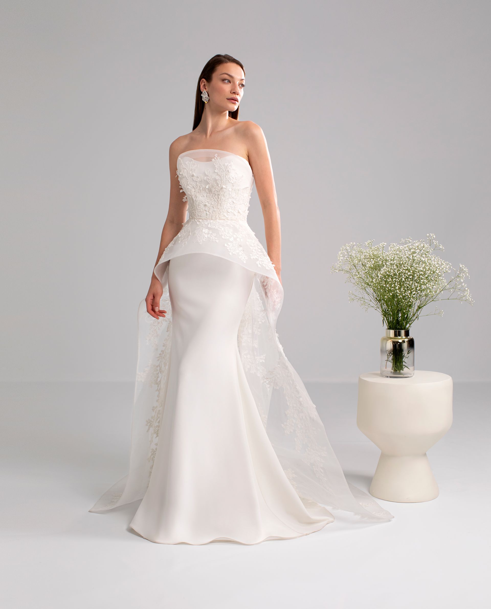 Donna in abito da sposa bianco senza spalline, con decorazioni floreali e strascico staccabile.