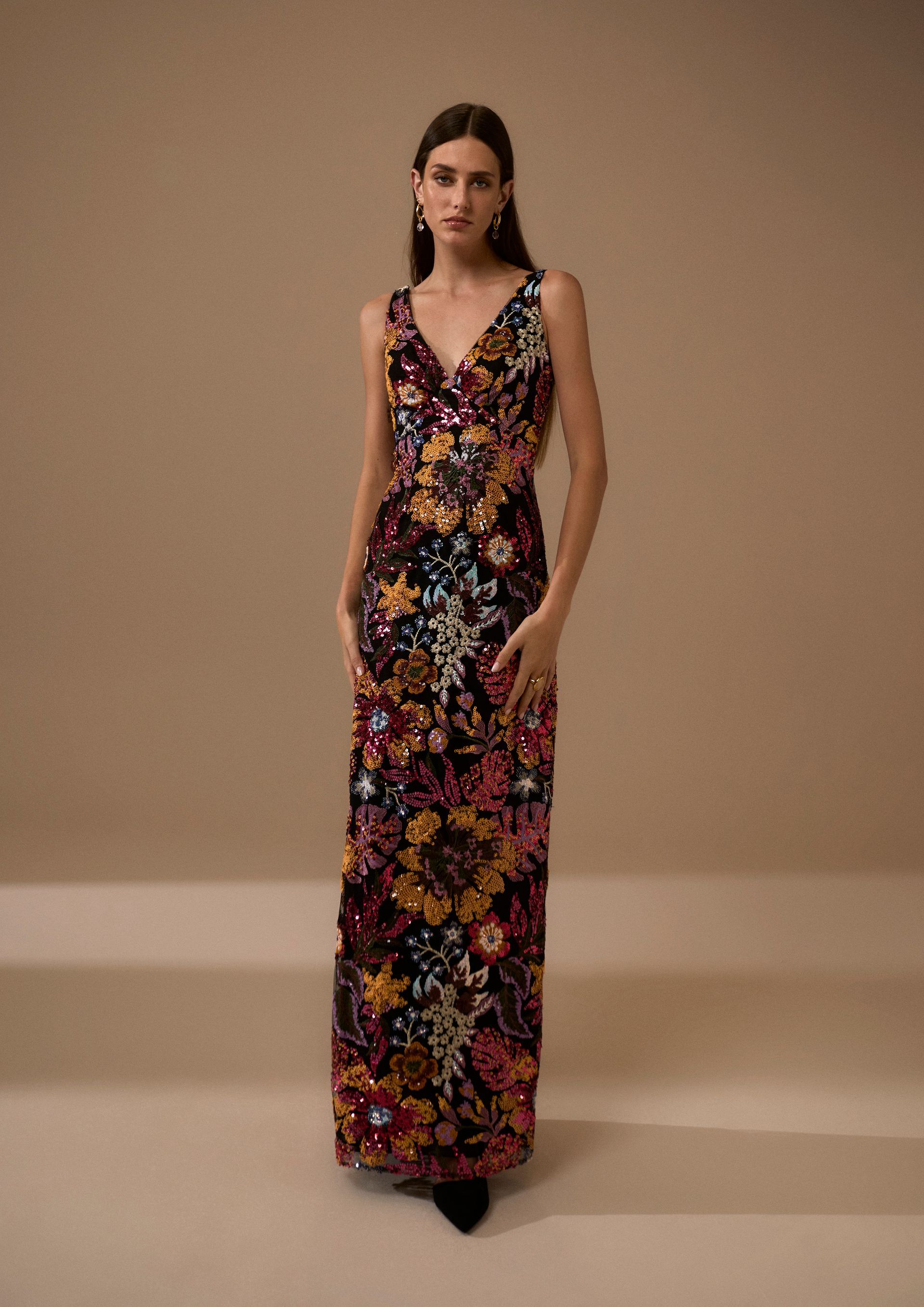Donna che indossa un abito lungo fino ai piedi con paillettes floreali. È in piedi in uno studio con uno sfondo neutro.