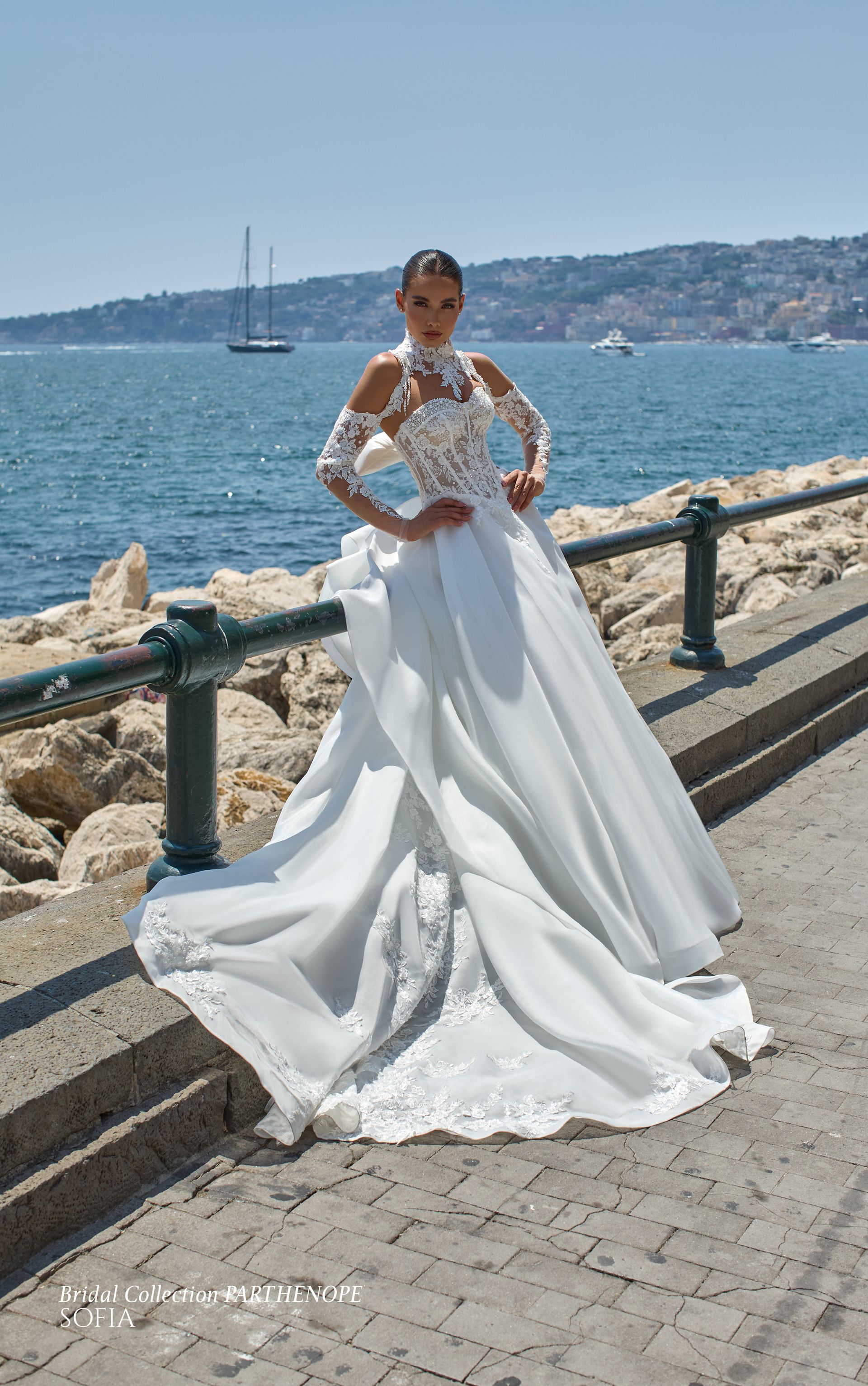 Una donna in abito da sposa bianco posa su un sentiero di pietra in riva al mare.