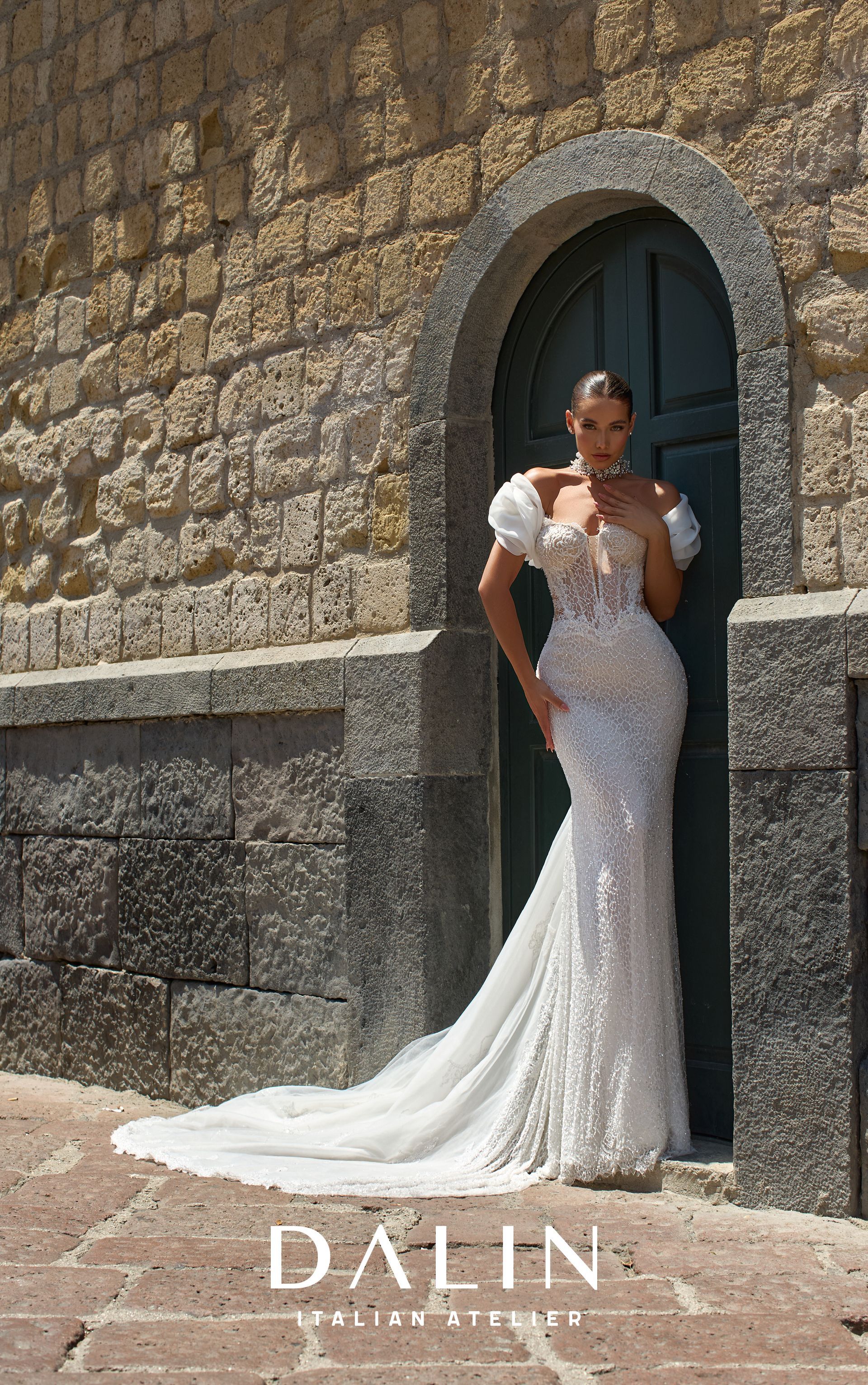 Una donna con un abito da sposa bianco con paillettes e strascico posa su una porta con un arco in cima