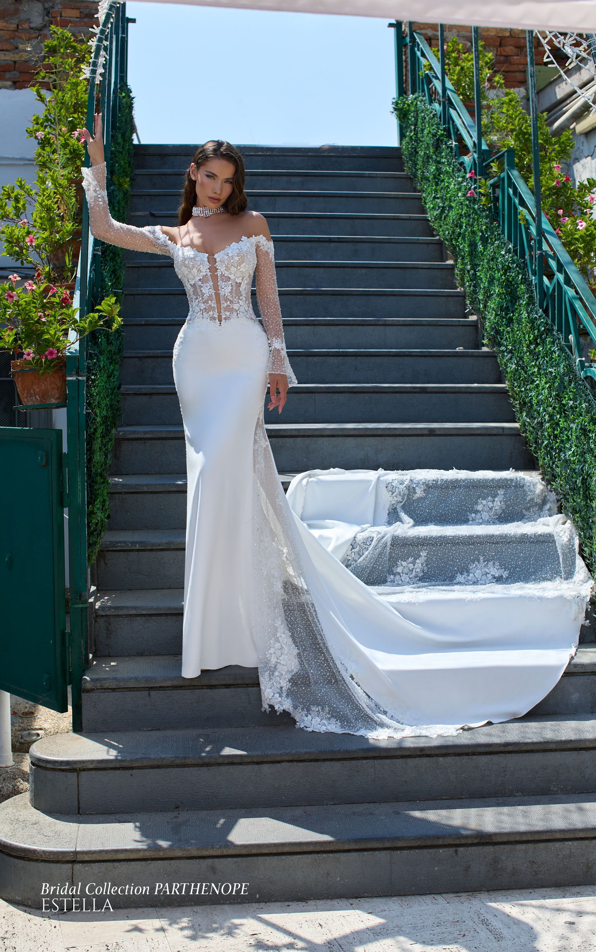 Una donna in abito da sposa bianco con lungo strascico posa sui gradini esterni.