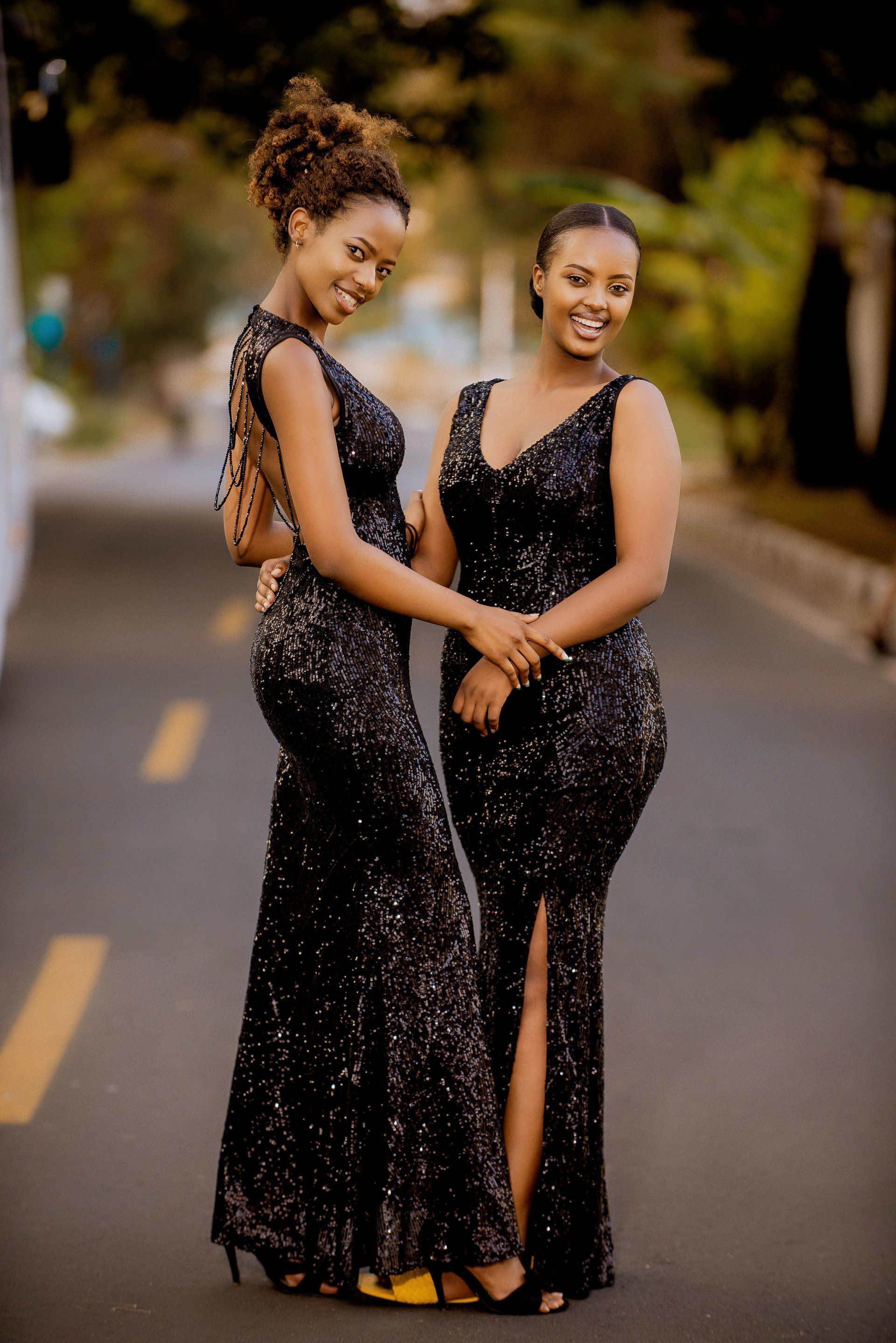Due donne in scintillanti abiti neri, sorridenti, in piedi su una strada.