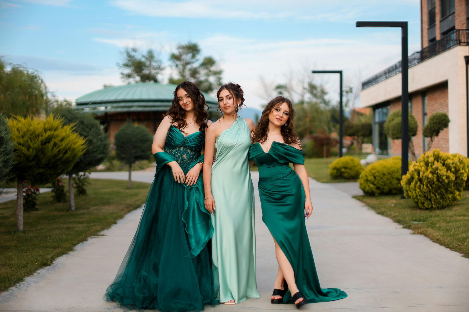 Tre donne in abiti color verde acqua posano all'aperto su un sentiero.