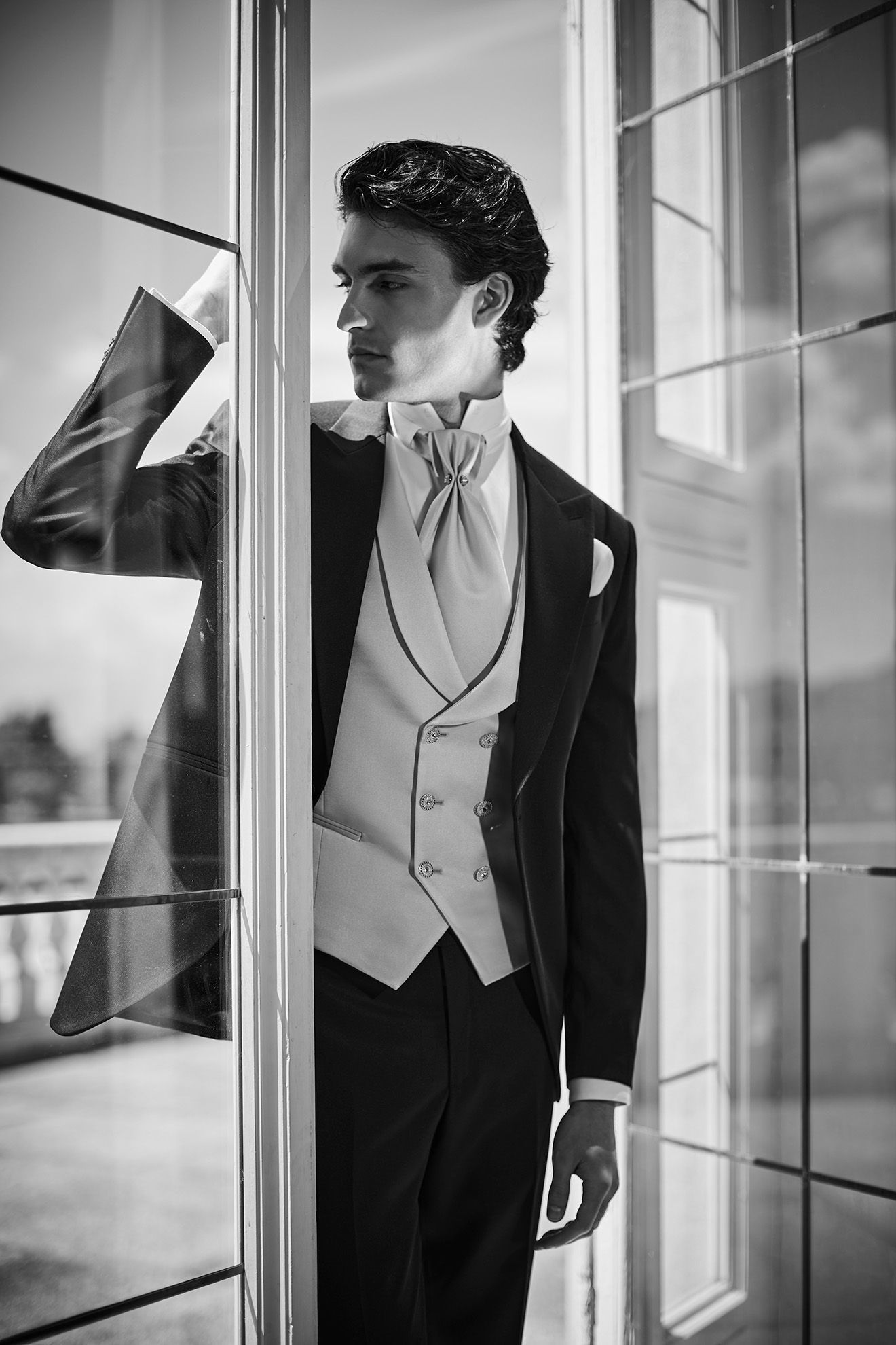 Uomo in abito formale, appoggiato alla porta, guarda altrove, bianco e nero.