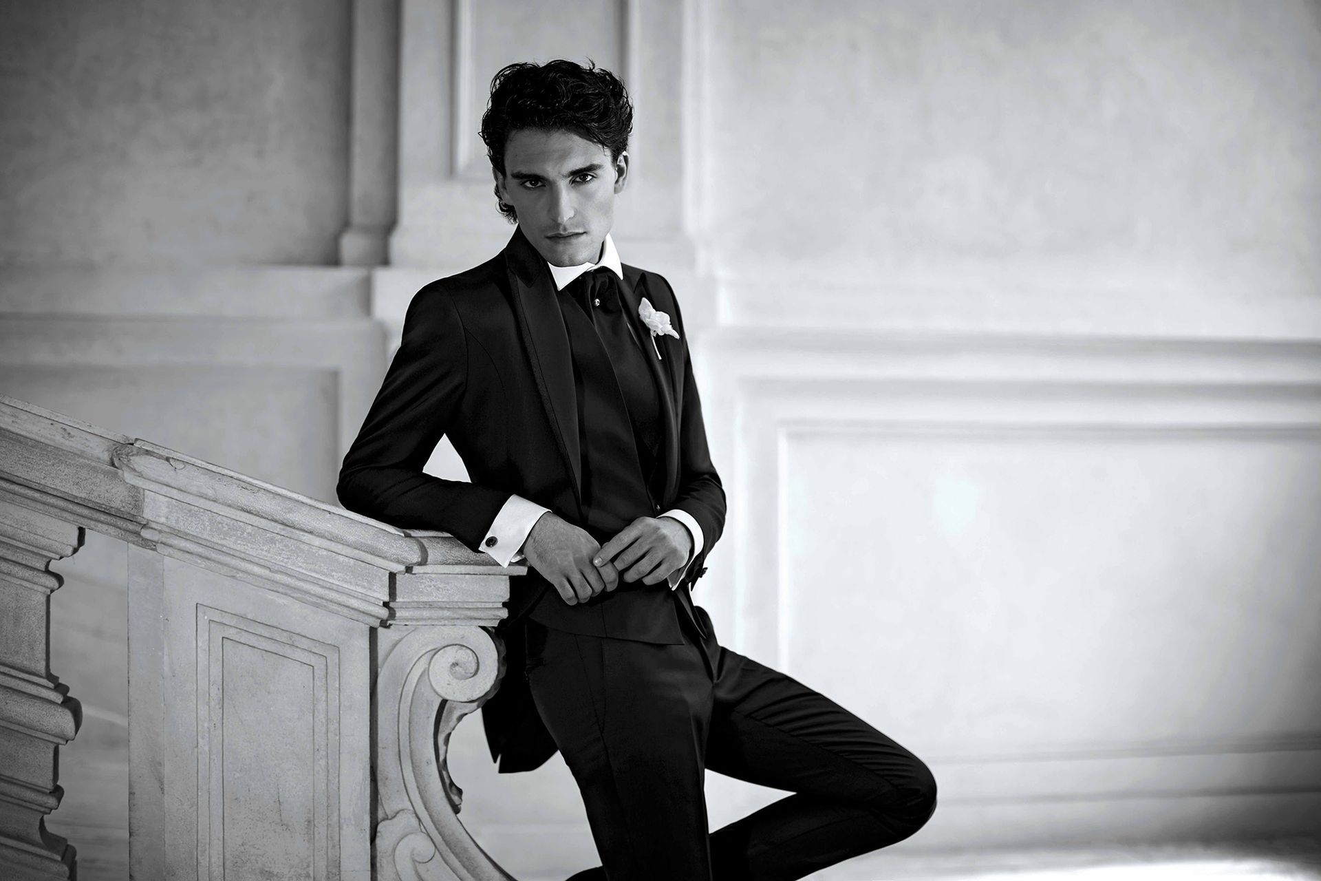 Un uomo in smoking nero si appoggia a una ringhiera decorata.