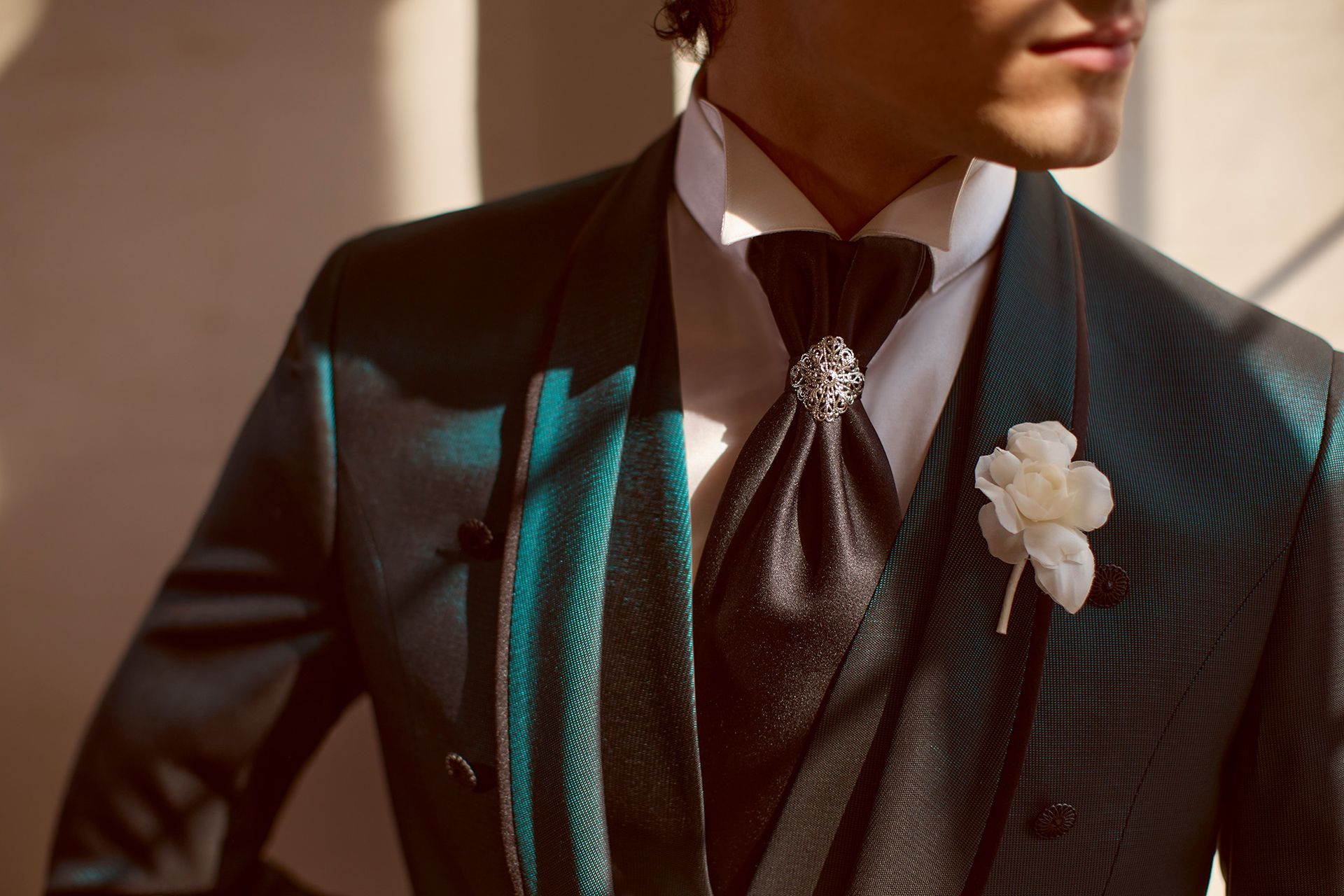 Uomo in abito verde scuro con drappeggio nero, camicia bianca e fiore all'occhiello.