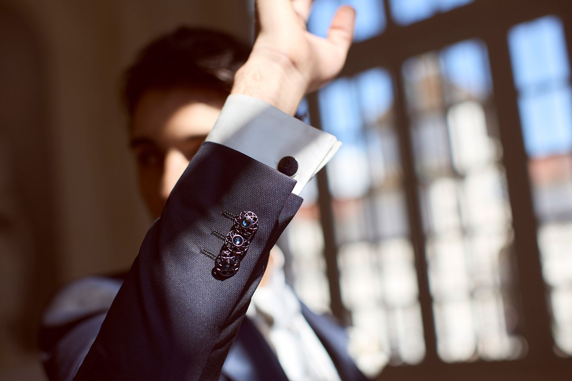 Braccio di un uomo in abito blu, con gemelli in mostra e camicia bianca; illuminazione interna soleggiata.