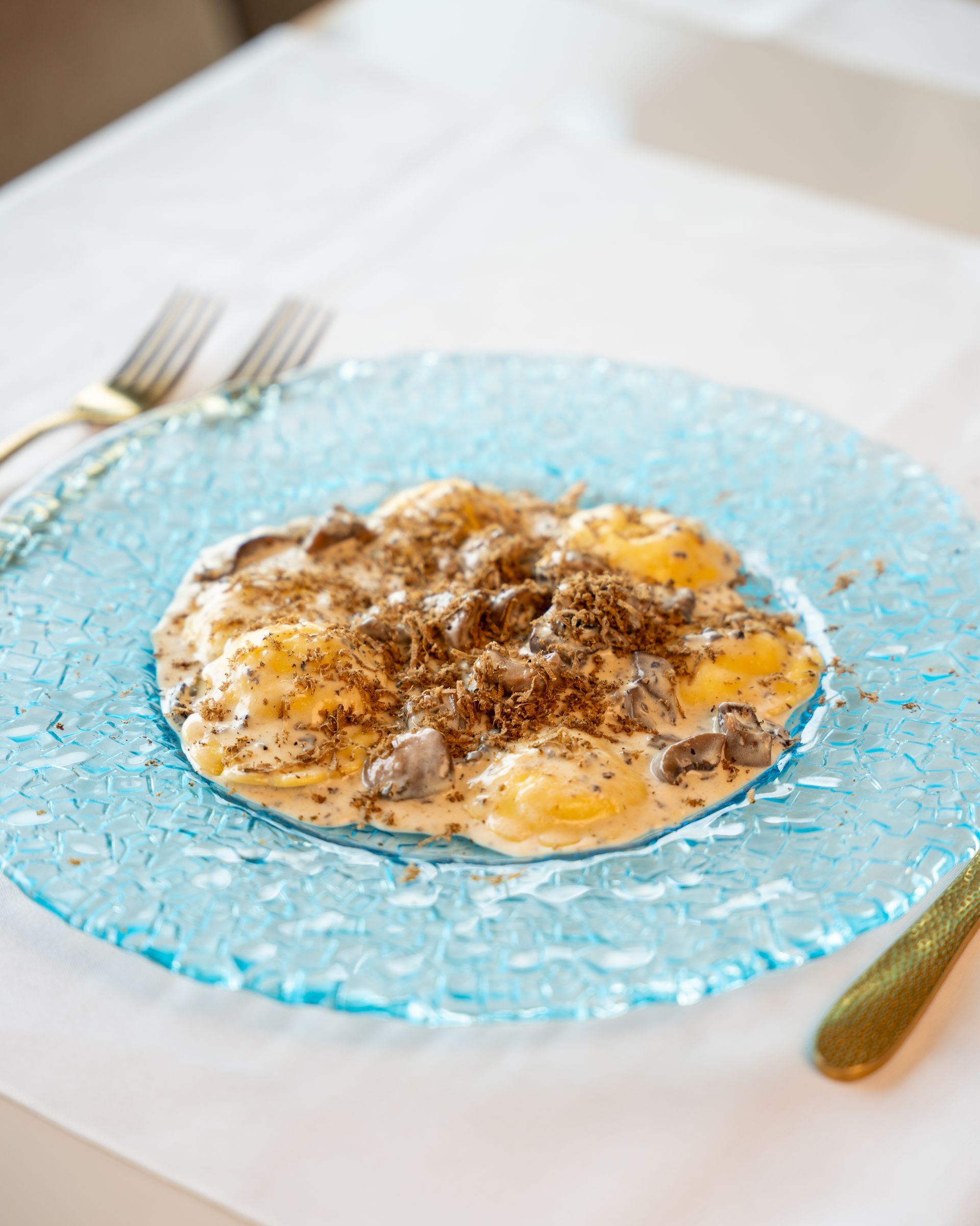 Pasta dish with truffles on a blue plate, set on a white tablecloth.