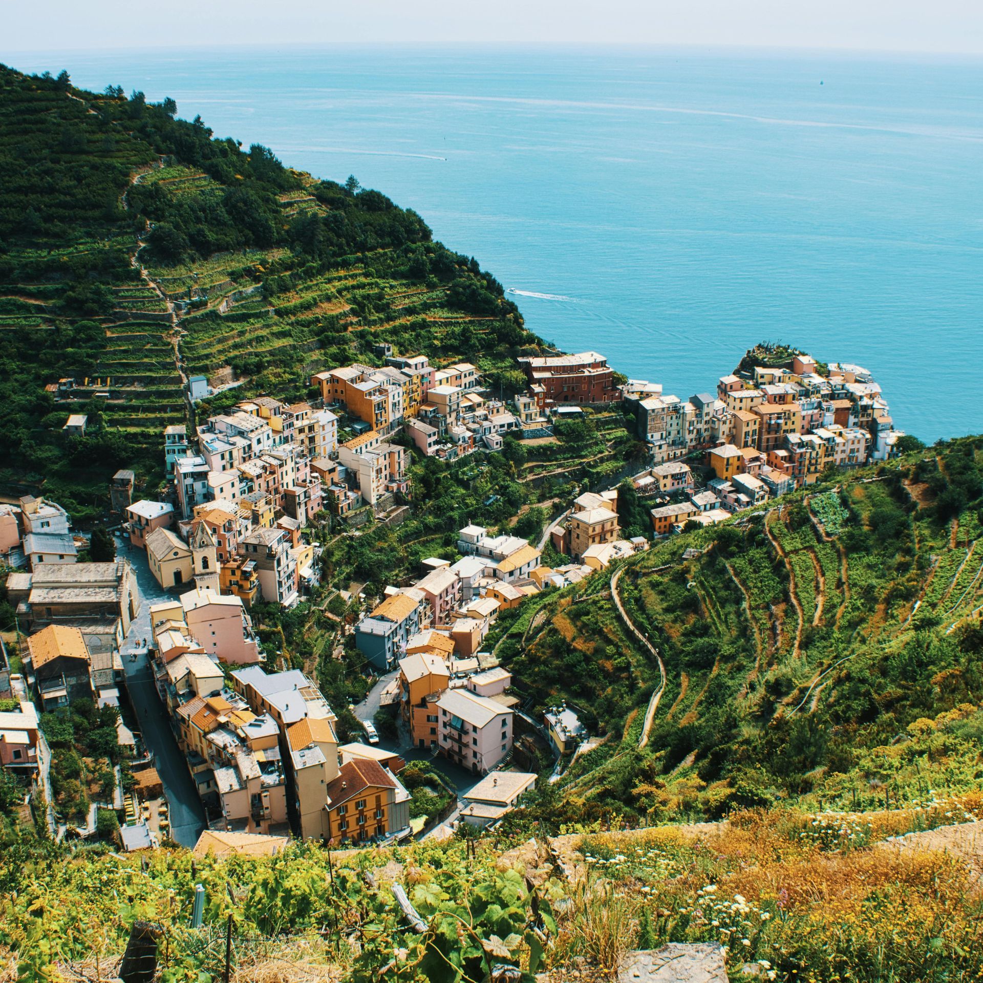 Coastal village nestled on a hillside, with colorful buildings, terraced farms, and the blue sea.
