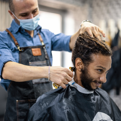 A man is getting his hair cut by a barber wearing a mask.