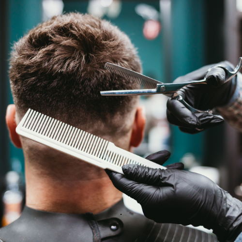 A man is getting his hair cut by a barber while holding a comb and scissors.