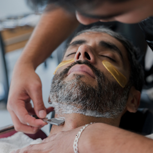 A man with a beard is getting his face shaved with a razor