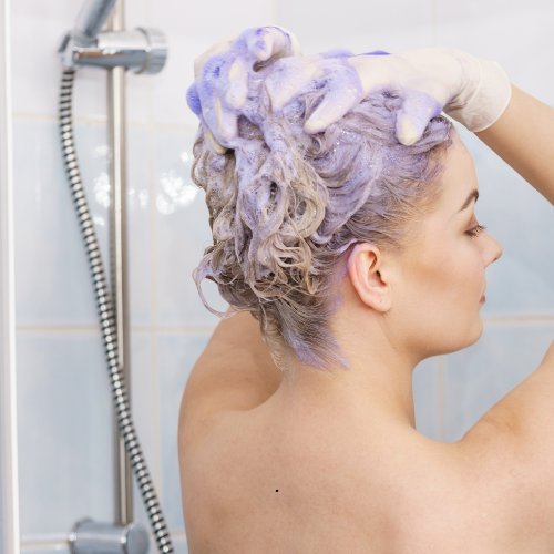 A woman is washing her hair with purple shampoo