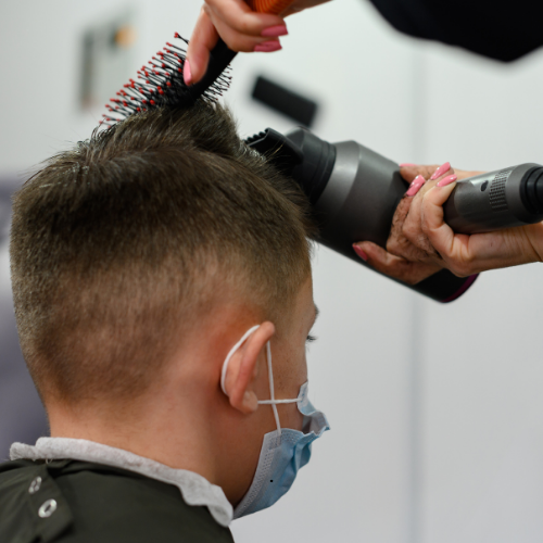 A man wearing a mask is getting his hair blow dried