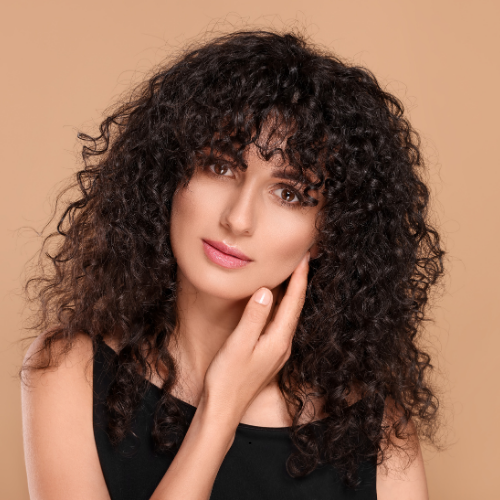 A woman with curly hair is touching her face with her hand.